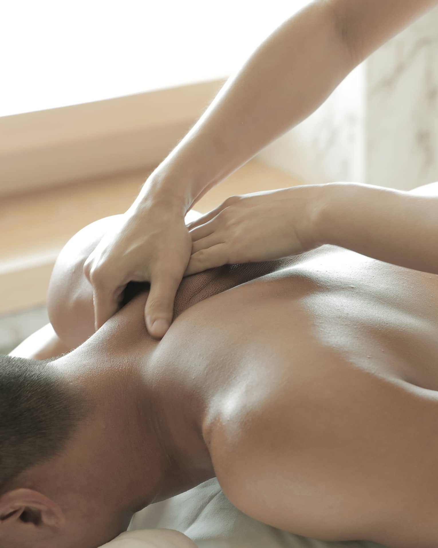 Spa masseuse massages man's bare back, shoulders