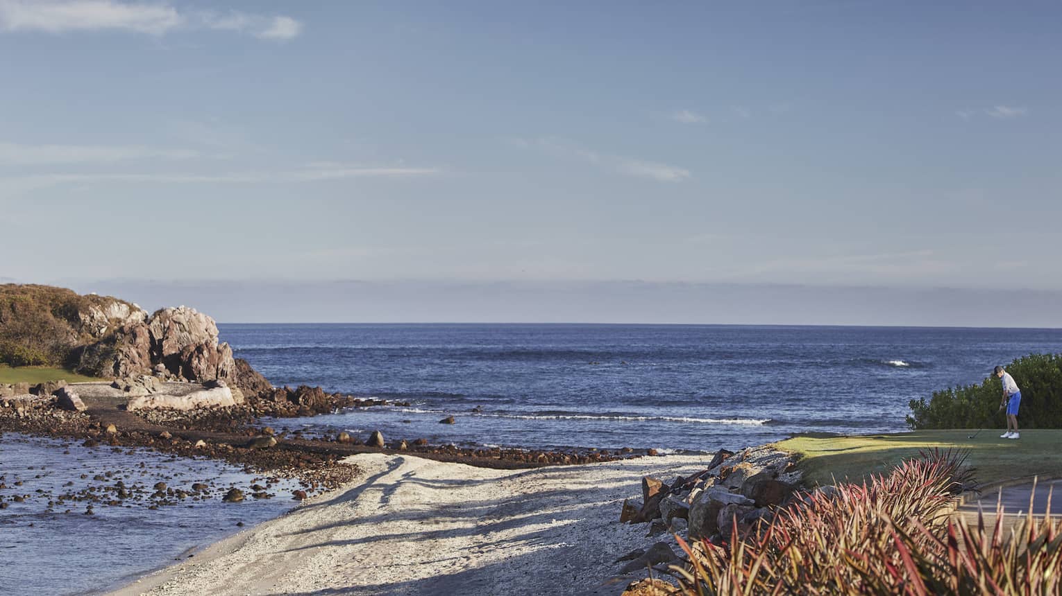 Sweeping view of golf course greens extending onto rocky island along coast