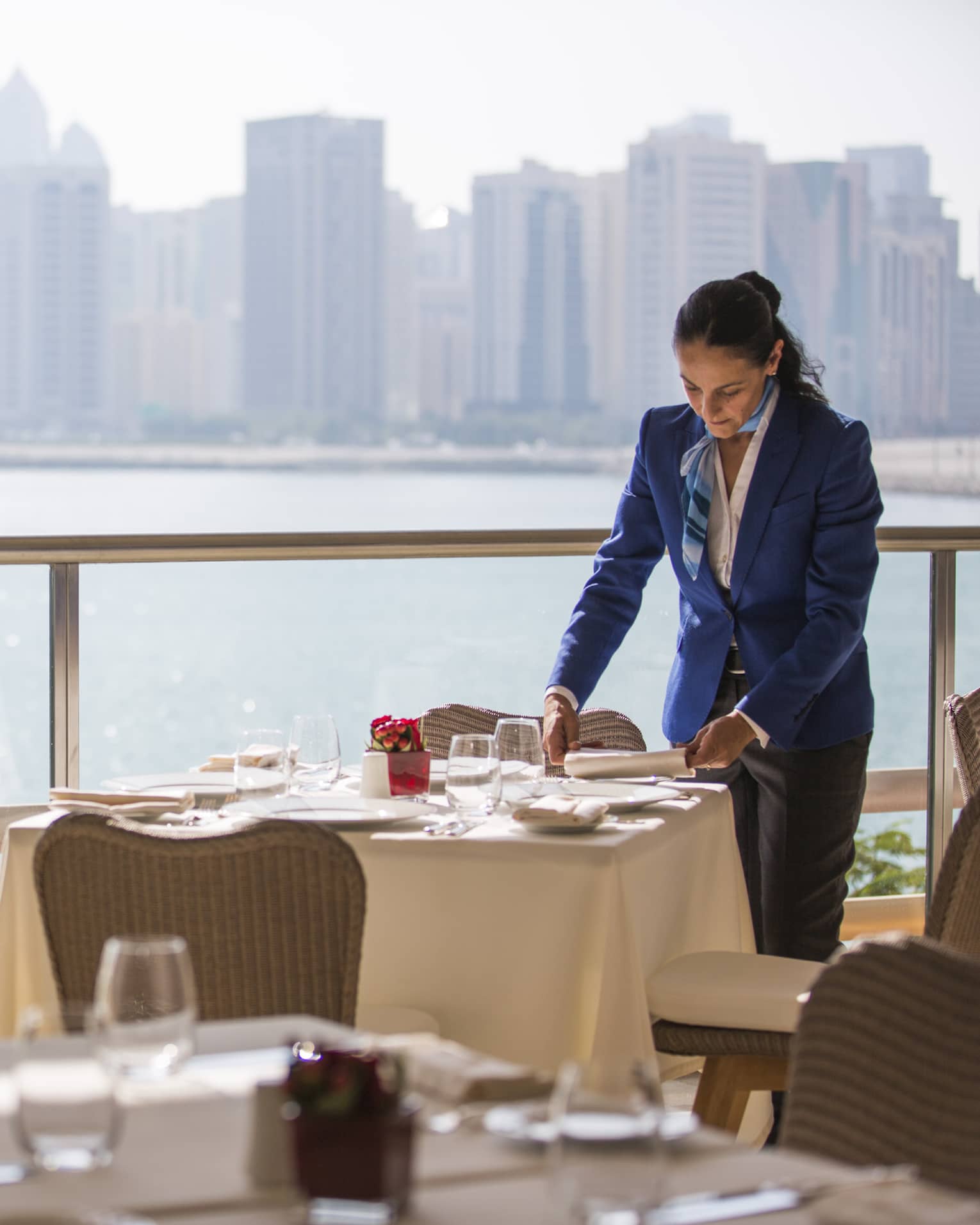 A four seasons staff setting an indoor  Cafe Milano table overlooking the water 