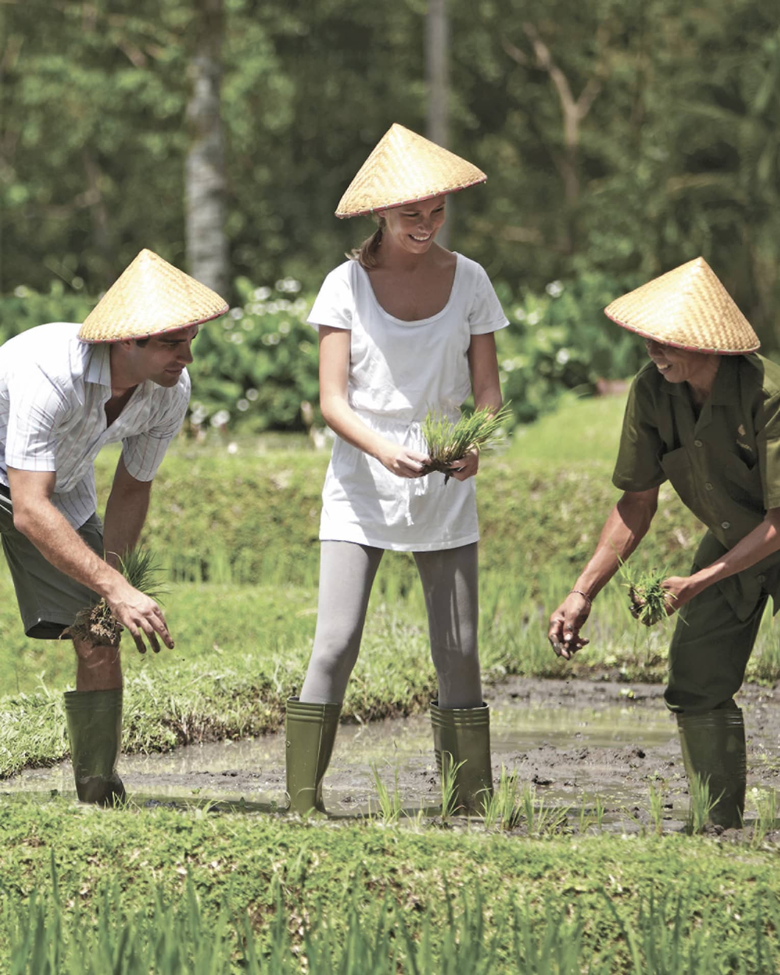 Man and woman in straw farmers hats kneel over garden, help gardener in rice paddie field