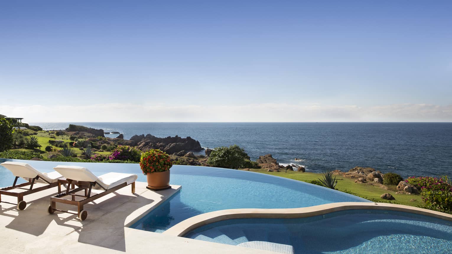 An outdoor terrace at an oceanfront villa in mexco with two lounge chairs and large infinity pool, with expansive sea views.
