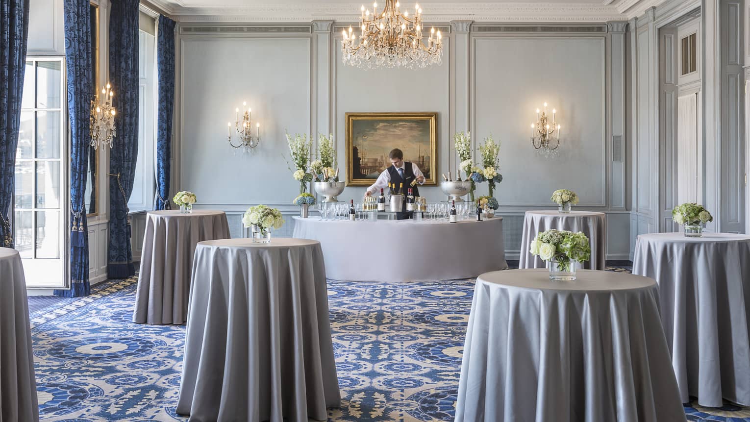 Bartender in event room with small cocktail tables, linens