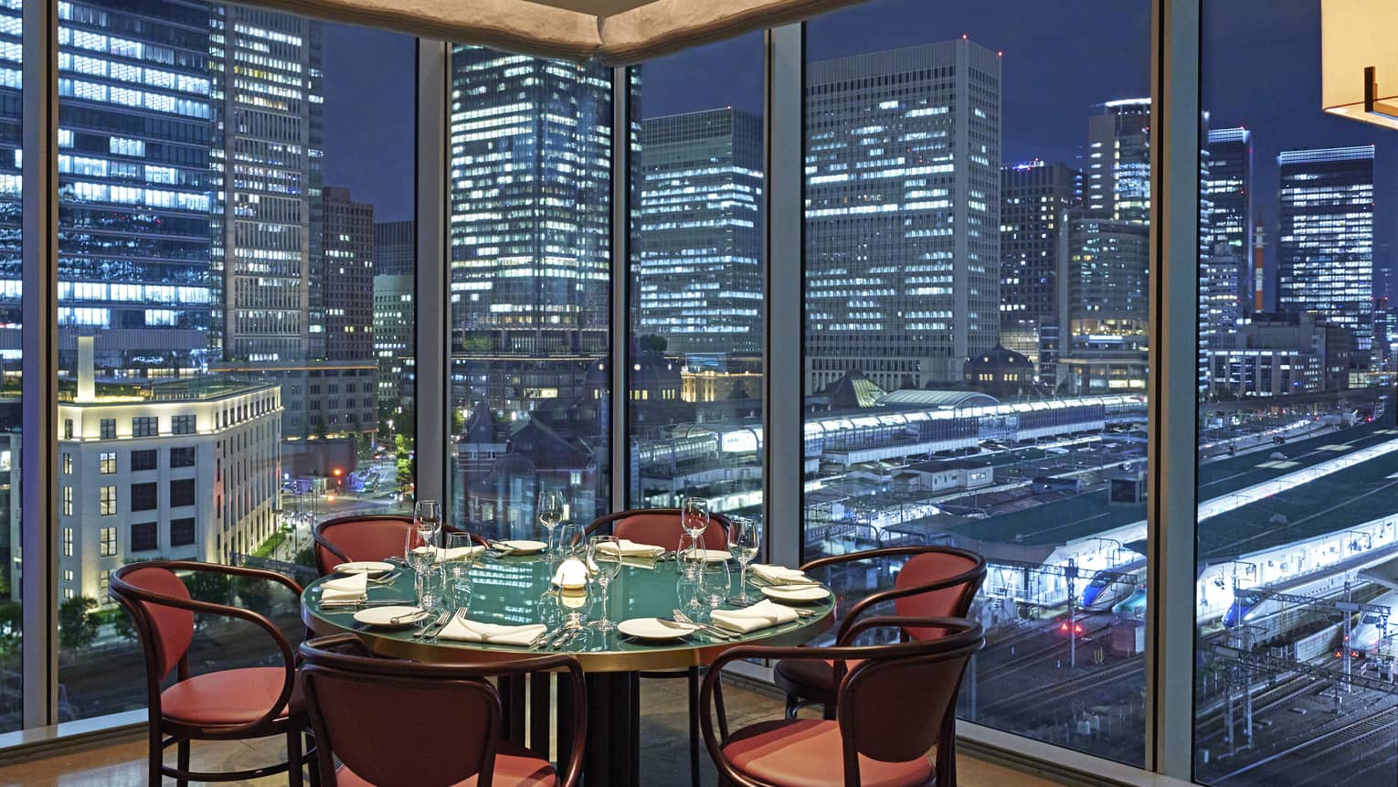 A round table and six chairs at Maison Marunouchi, floor-to-ceiling windows with views of downtown Tokyo at night