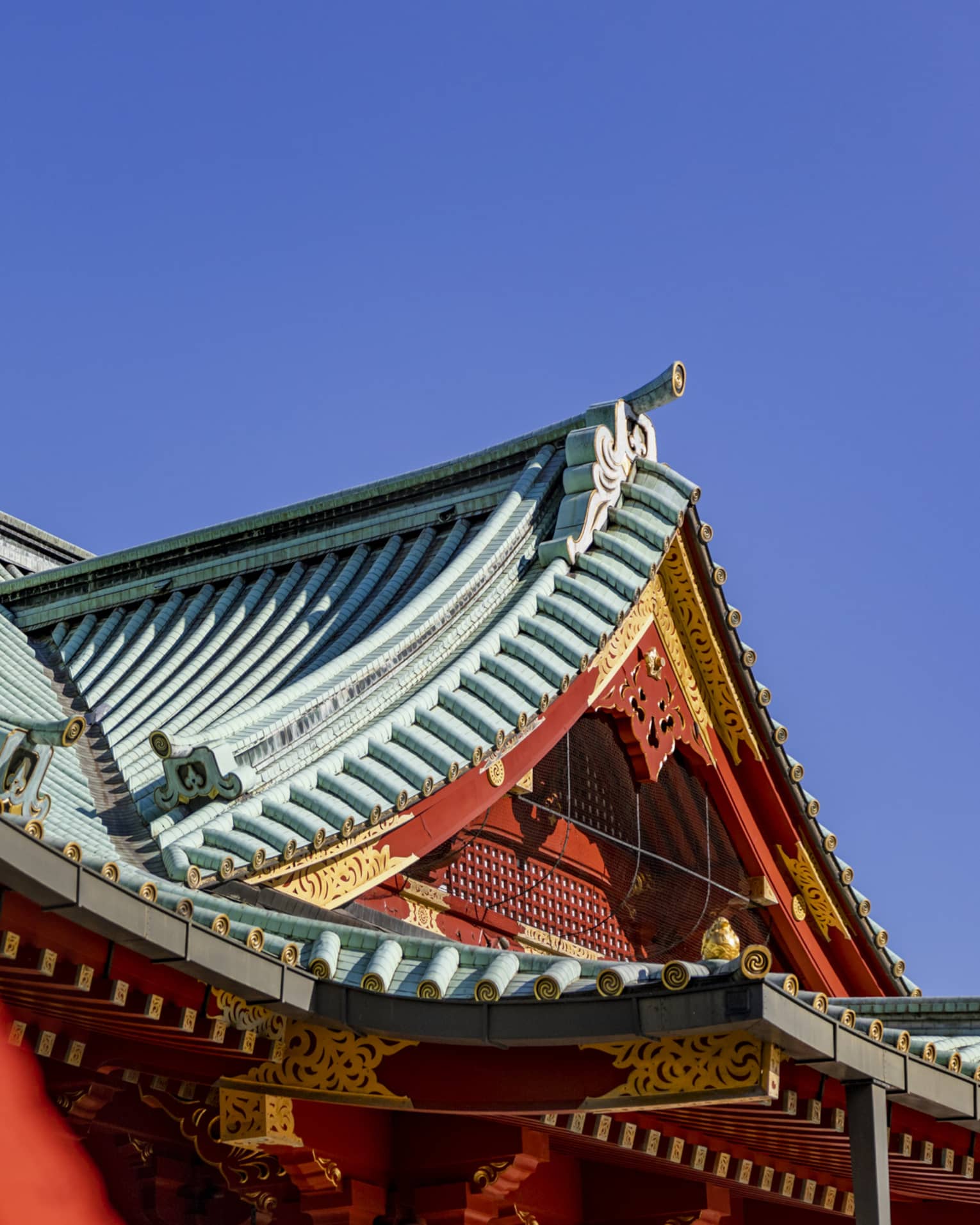 Concave tented gable rooftops of Shinto temples with ornate red and gold facades and grooved piping on the roofs.