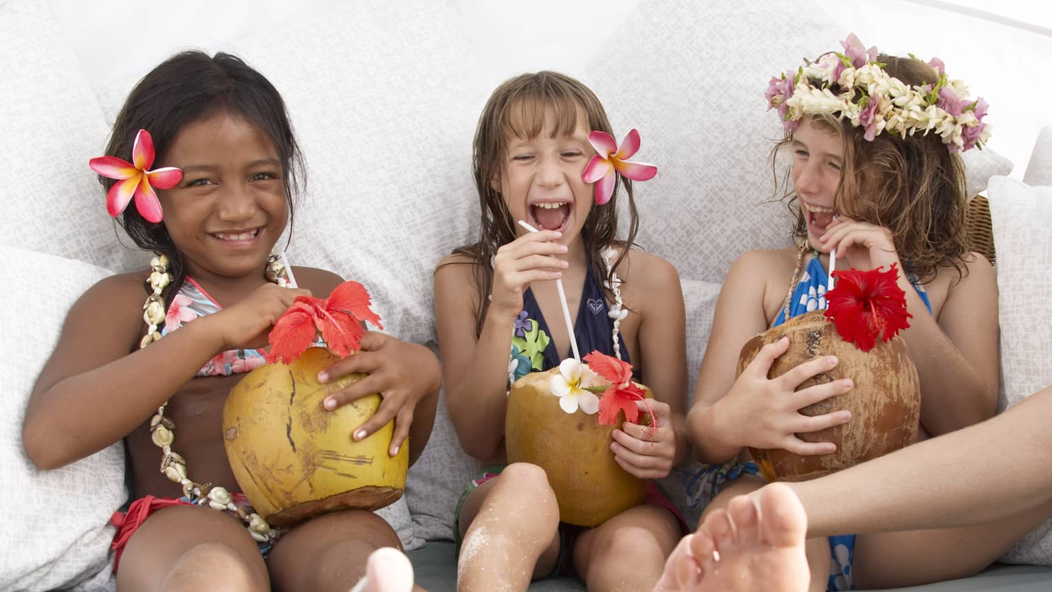 Three young girls laughing with tropical drinks, tropical flowers in their hair