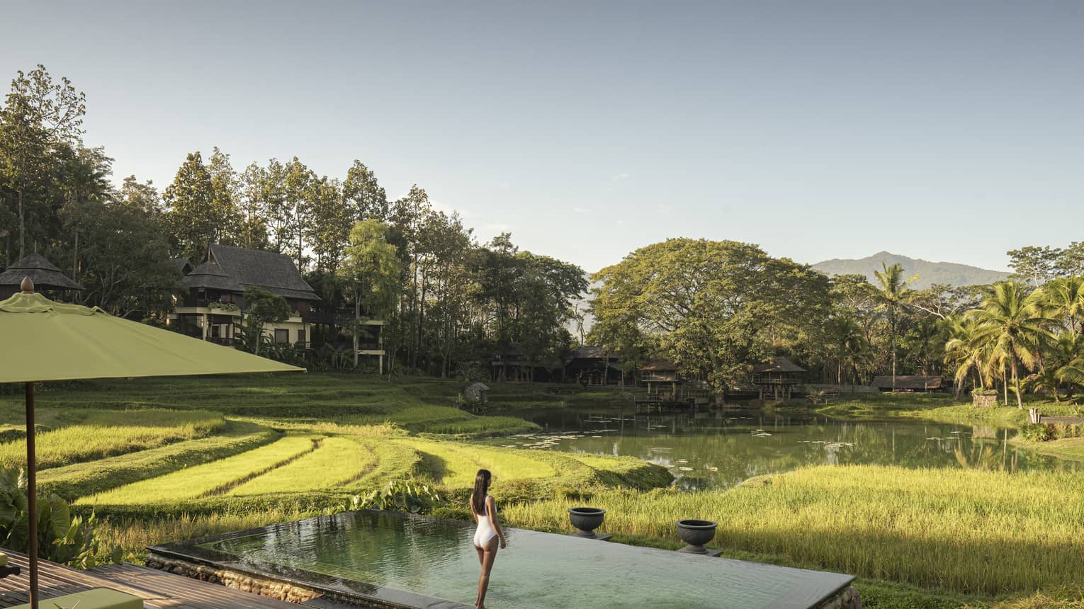 Woman in white bathing suit stands in front of pool overlooking rice paddies