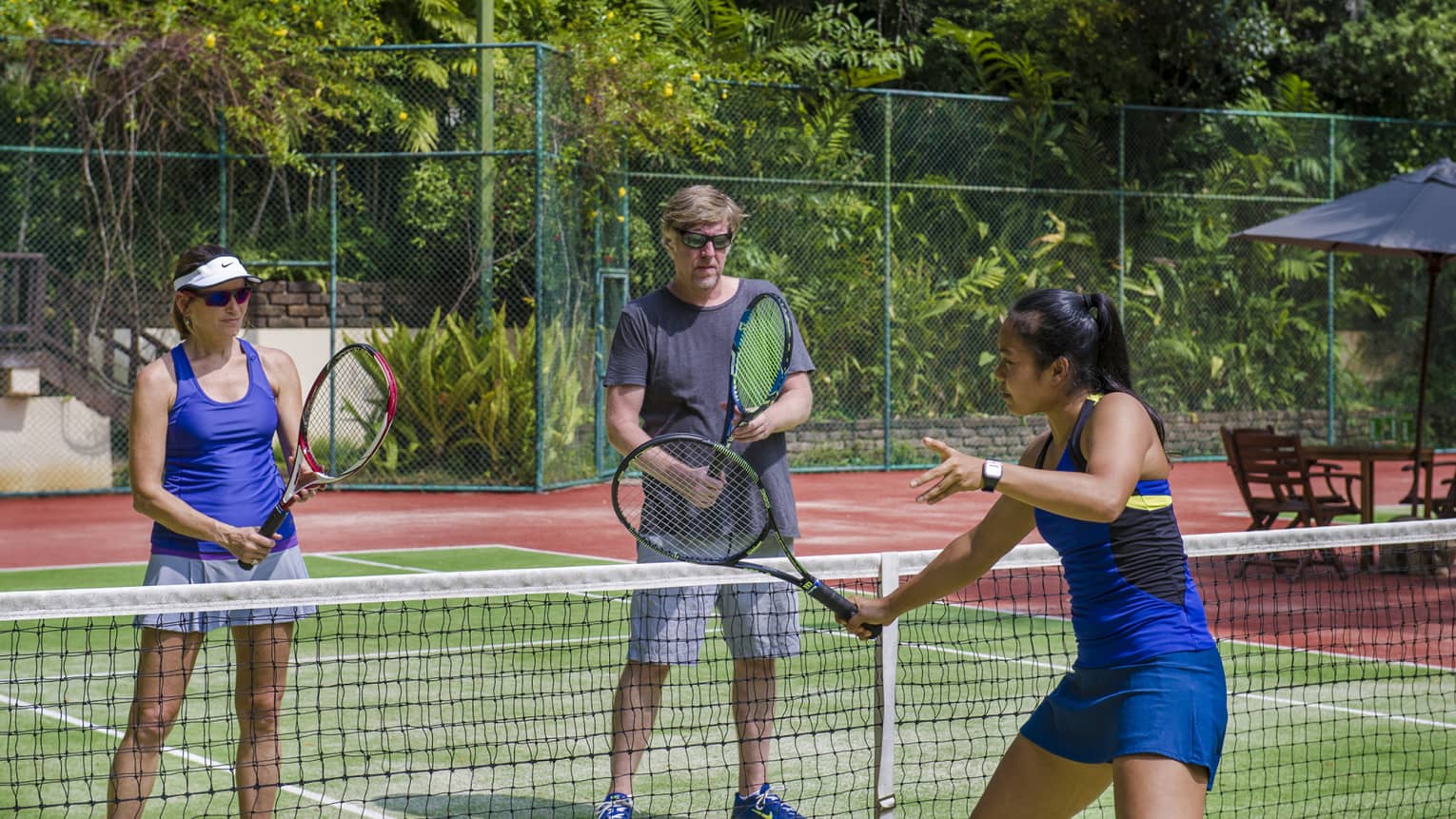Woman demonstrates tennis serve at net while tennis pro Nichapa Rungtein, woman watch