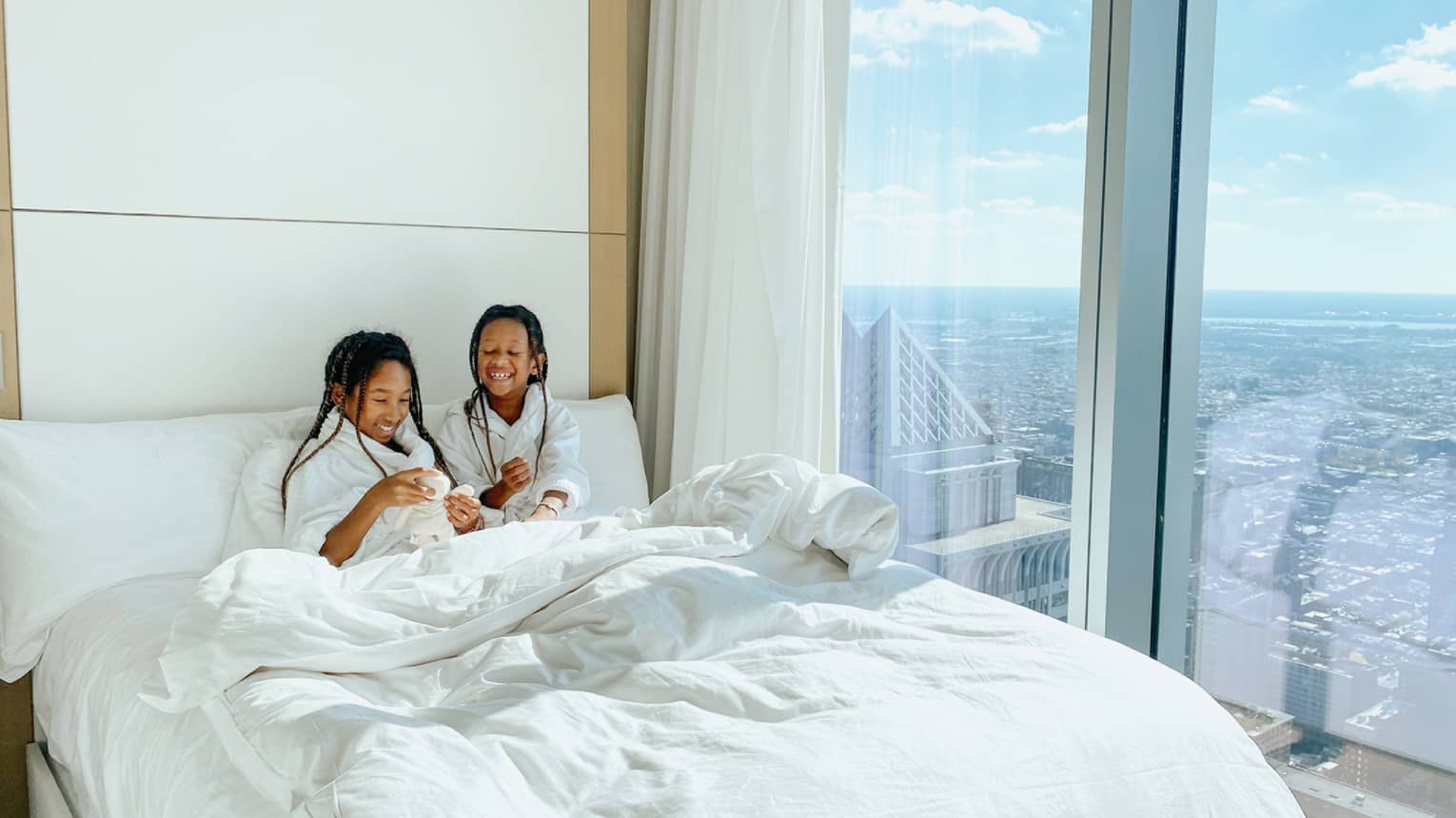 Two young girls relaxing in a bed with robes on.