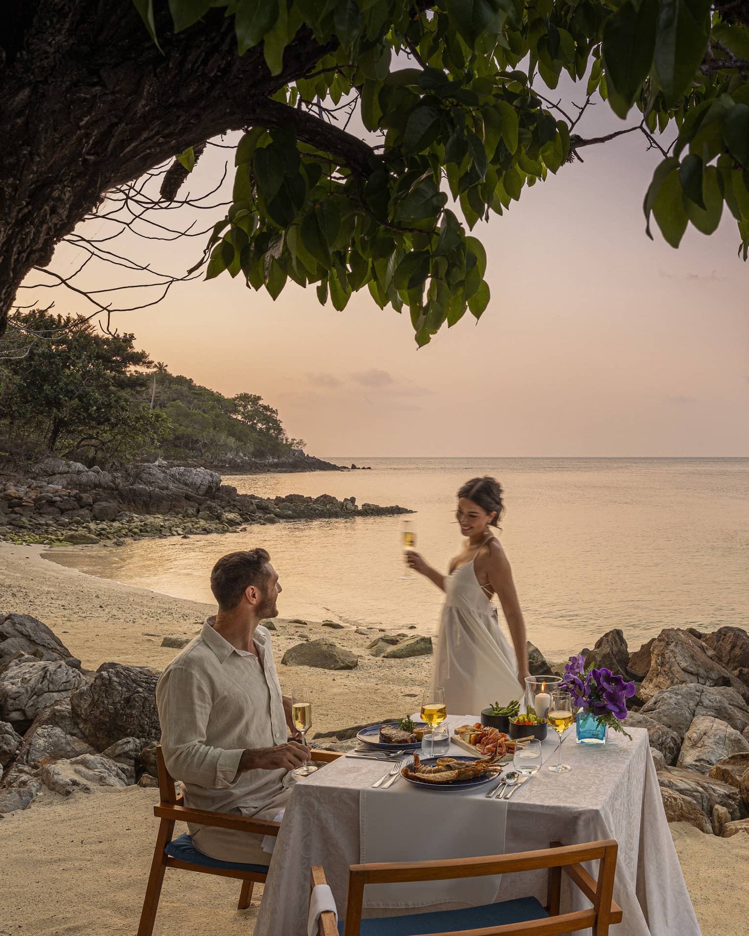 A beach dinner date at dusk, with a couple enjoying a serene seaside view.