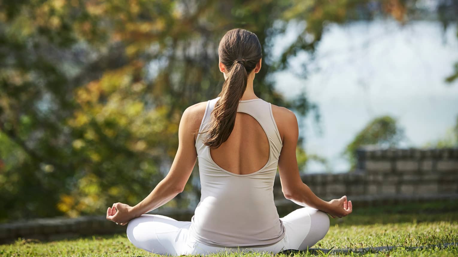 Back of woman meditating on sunny lawn