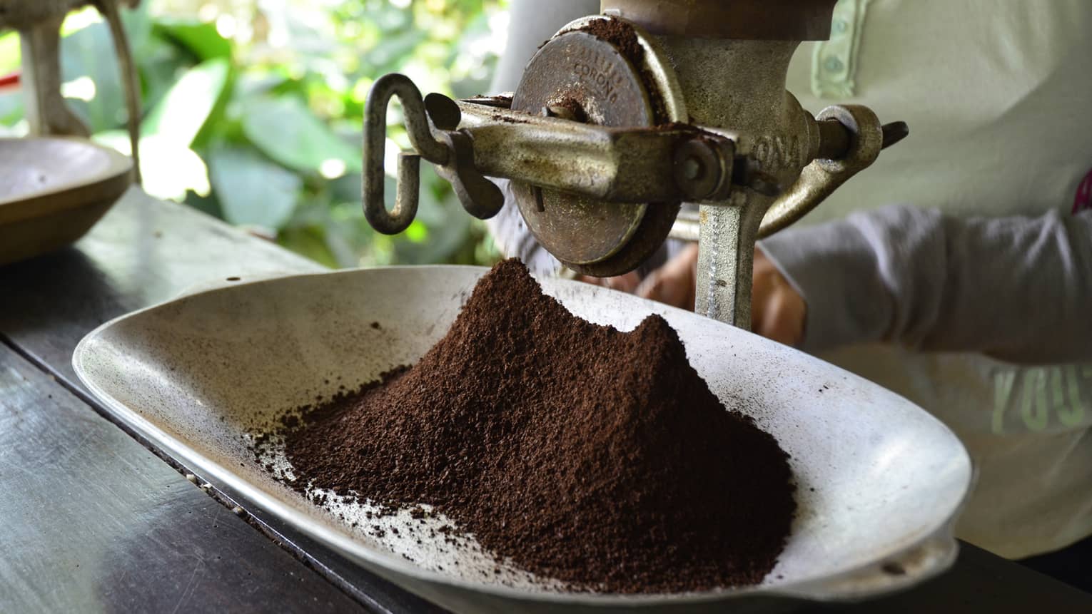 Large metal industrial-looking hand grinder with pile of ground Colombian coffee 