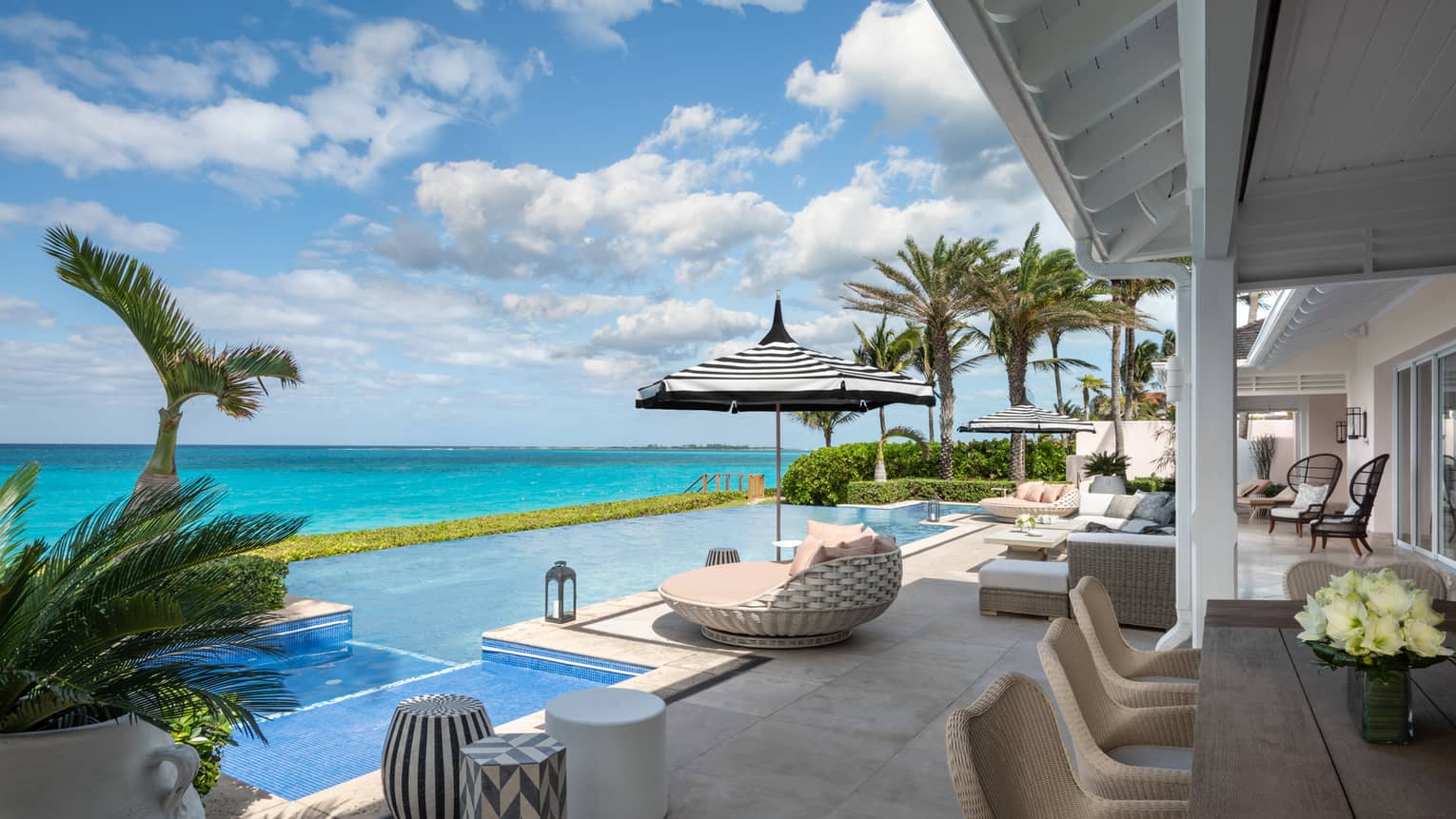 Beachfront villa residence terrace with private infinity pool, sun loungers, and ocean view under a bright blue sky