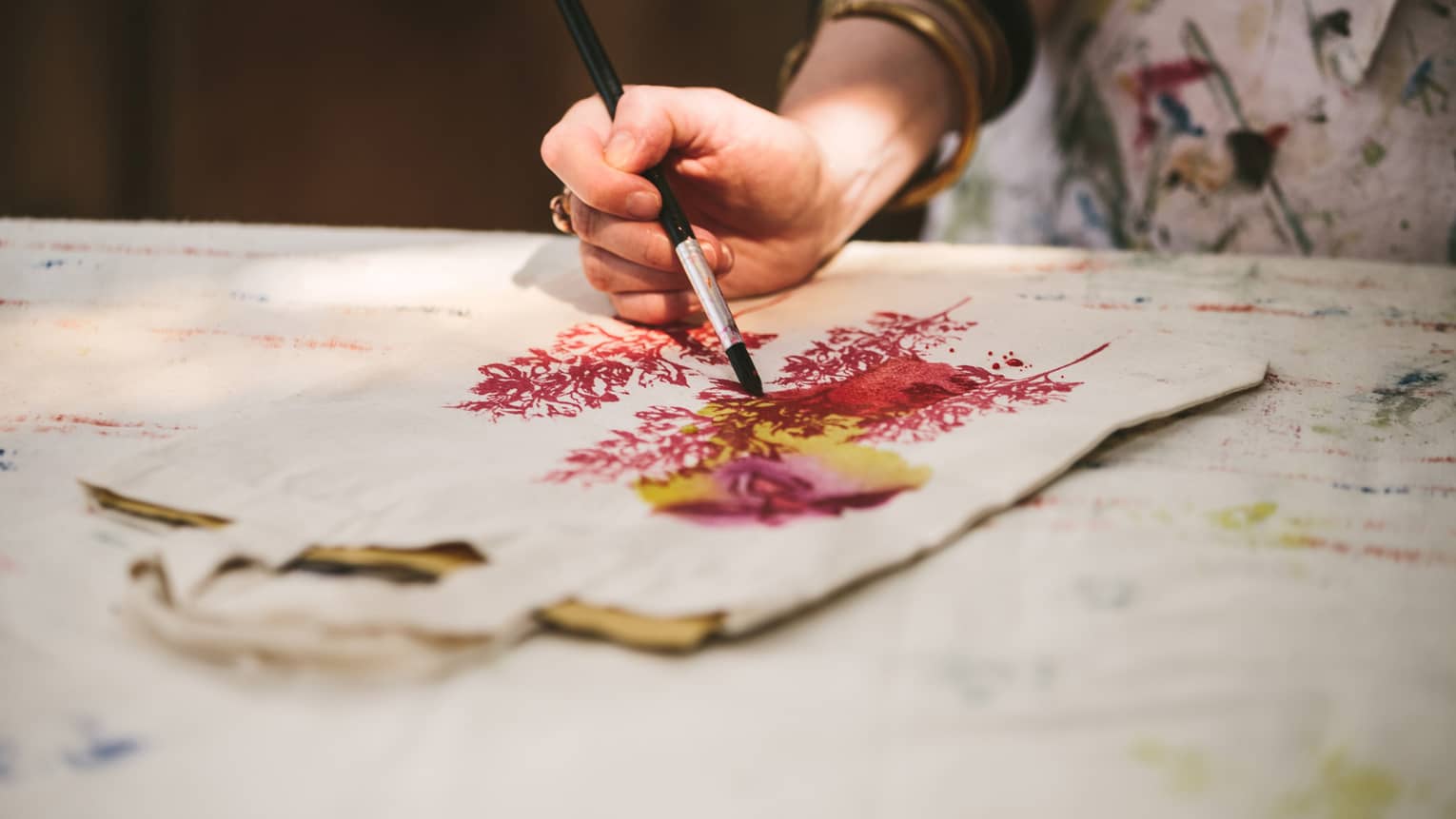 Close-up of woman with paint brushes painting flowers on canvas bag