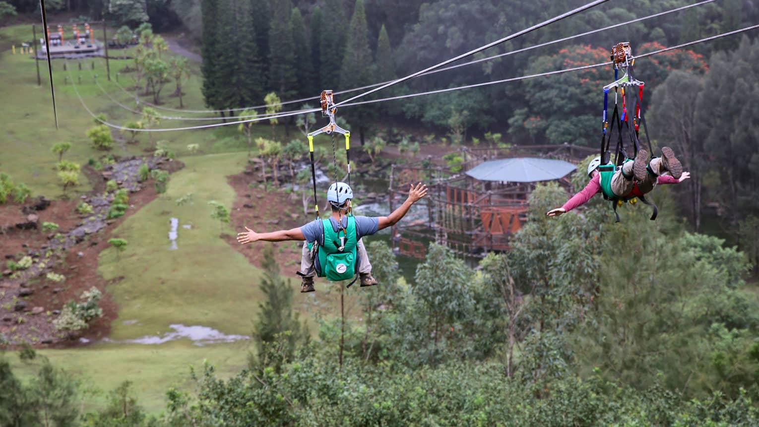 Adventure Park, two people glide down zip lines high above trees over mountain