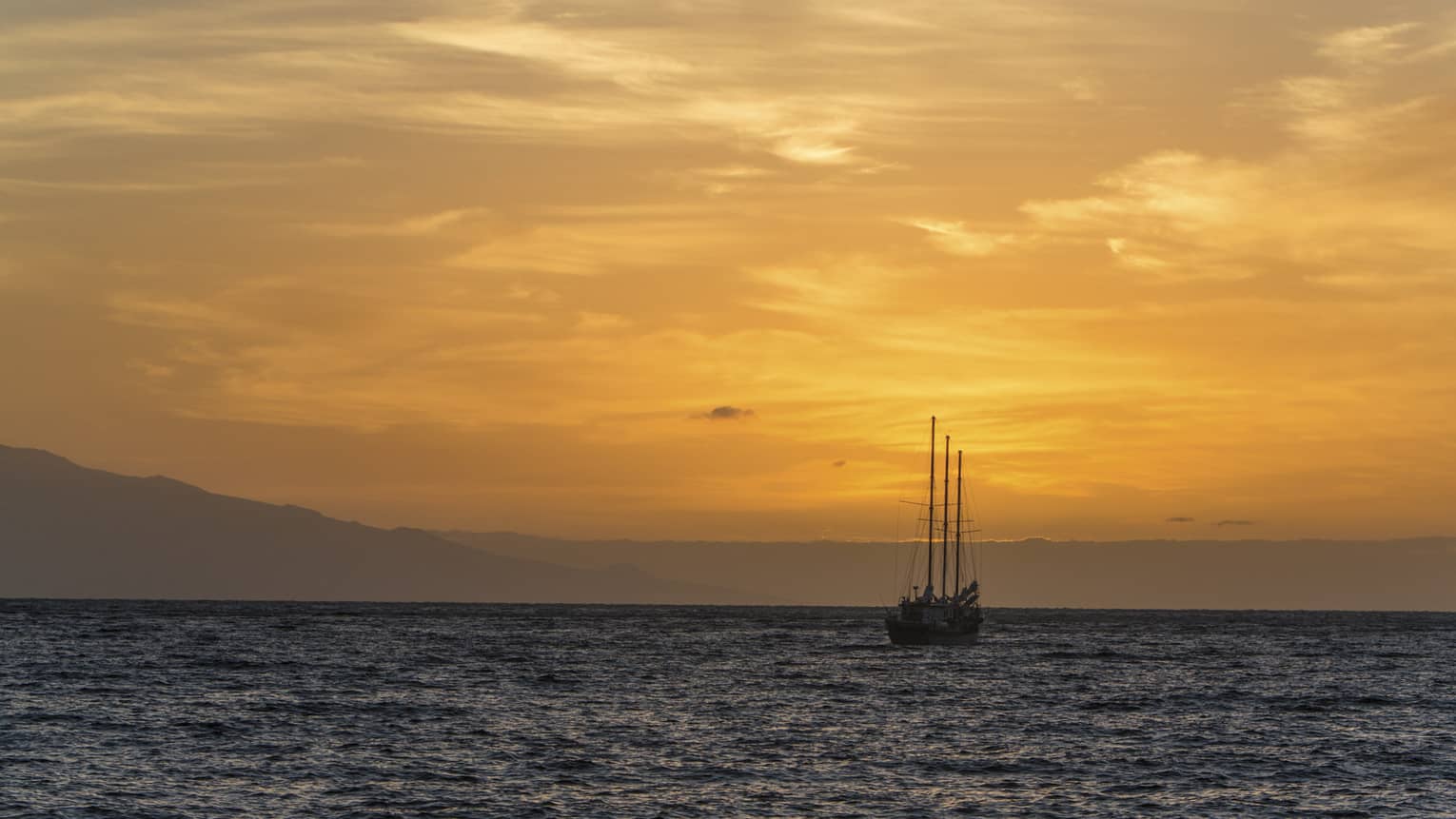 Sailboat silhouette on ocean against orange sunset