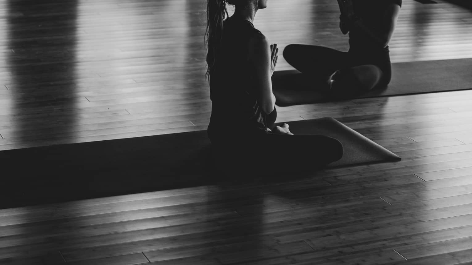 A black and white image of two women practicing yoga in a studio.