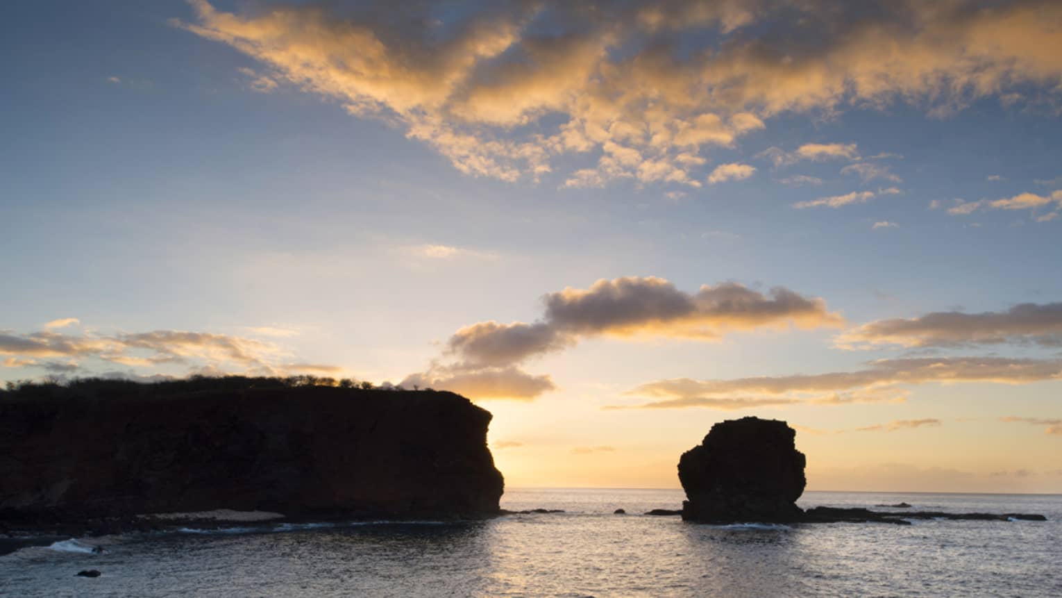 Silhouettes of islands on ocean against sunset