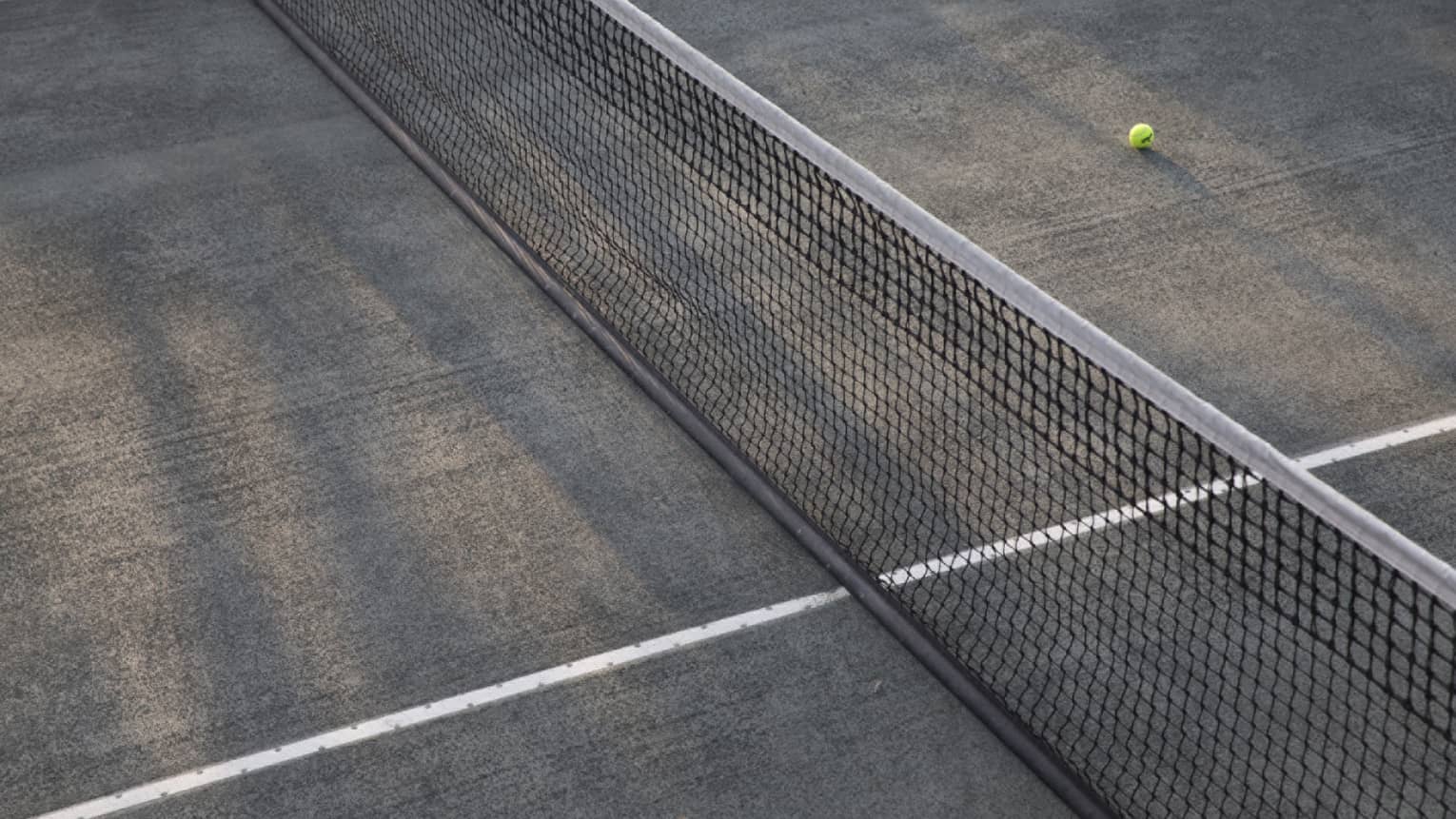 A lone tennis ball lies near the net on an empty court