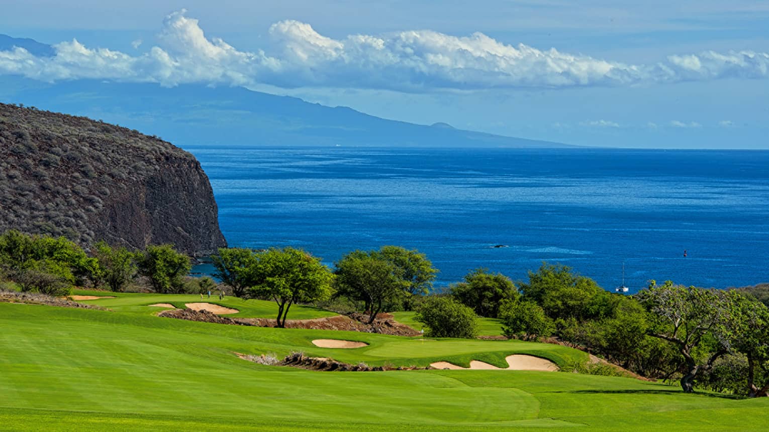 View over green golf course lawn, trees and cliff over ocean