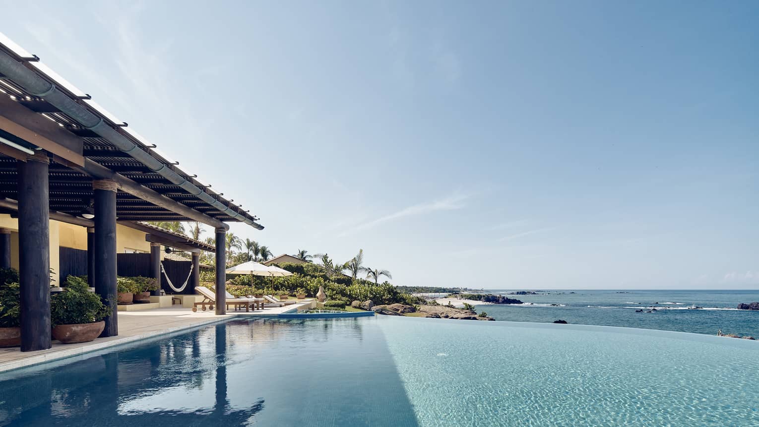 View over infinity swimming pool looking over ocean, covered patio at side