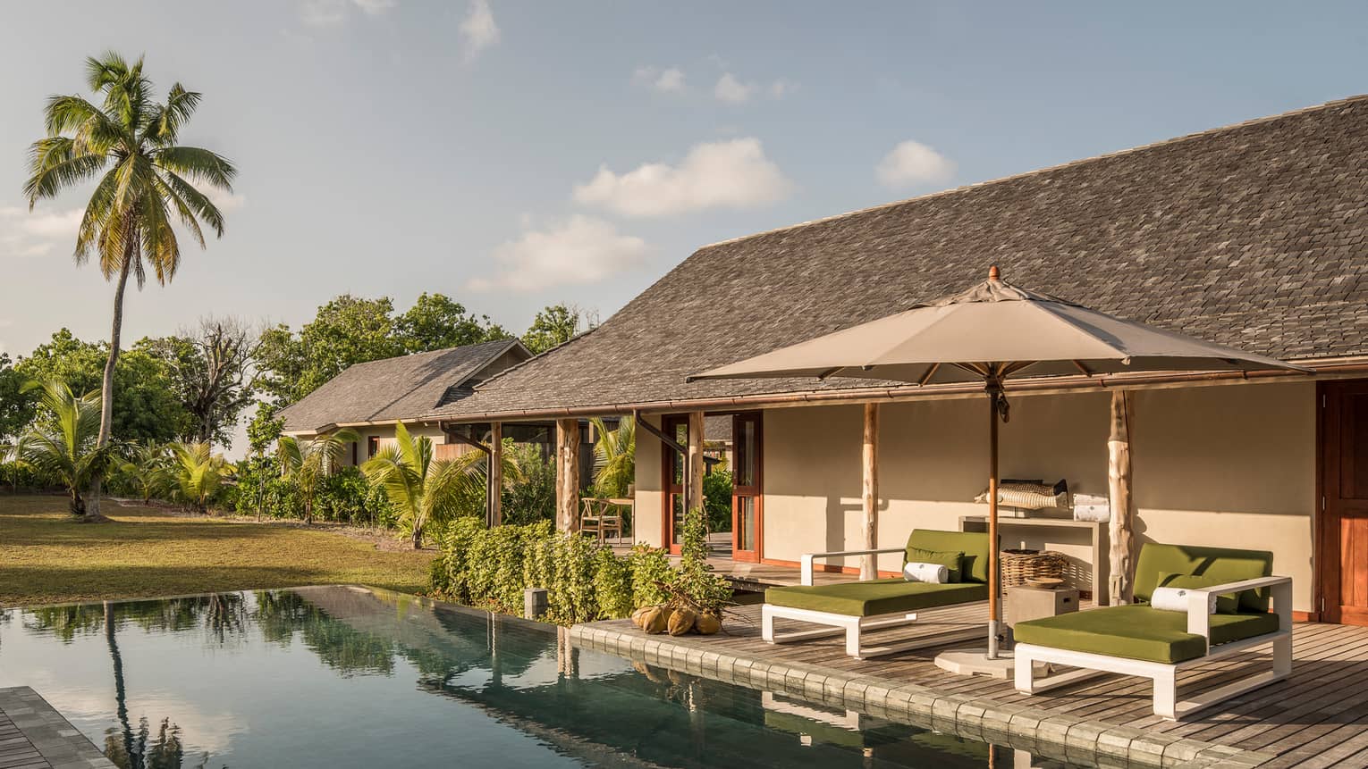 Palm tree reflecting on plunge pool under bungalow small patio with two lounge chairs, umbrella