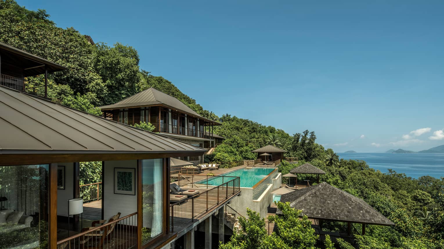 Four-Bedroom Residence Villa roofs, patios amid trees on mountain, ocean below