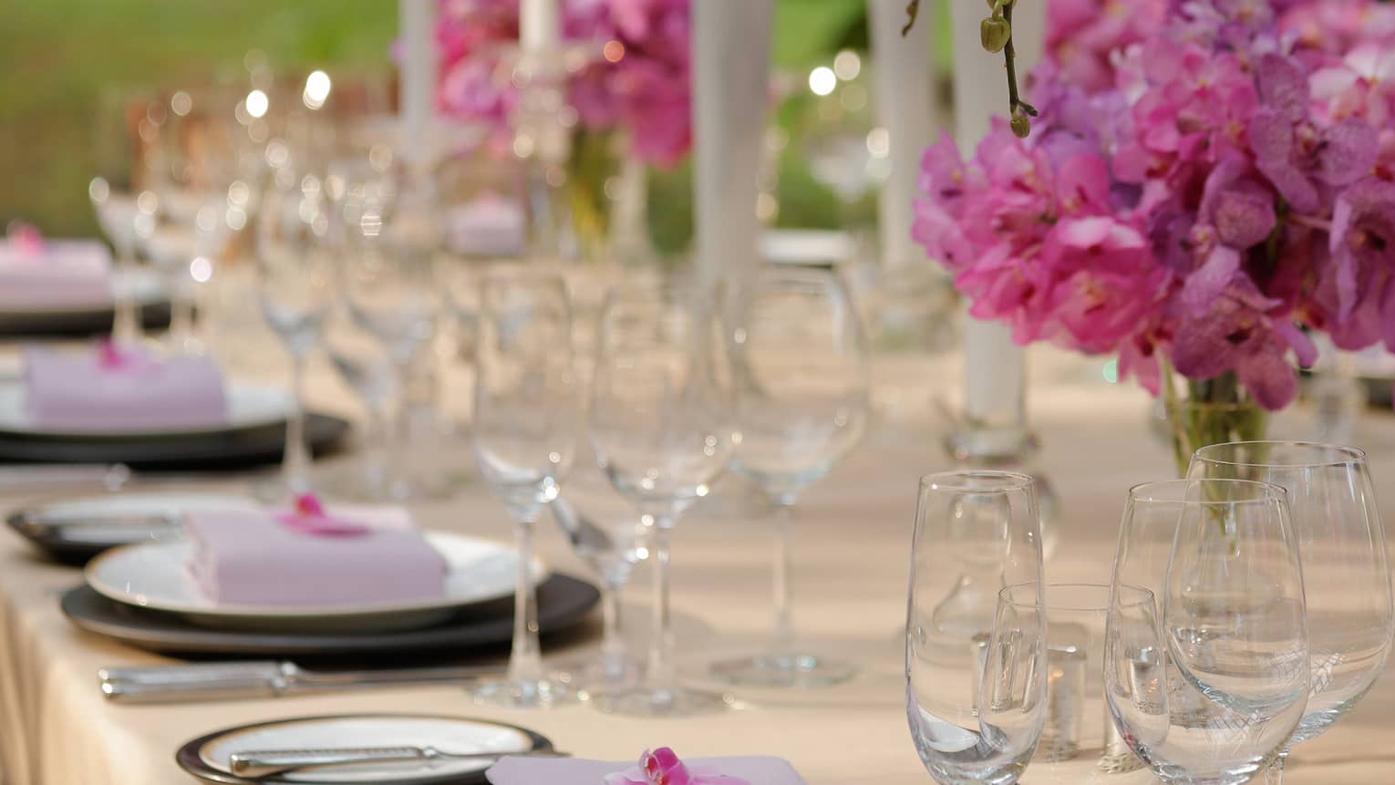 Outdoor dining table with pink flowers in vases, tall white candles 