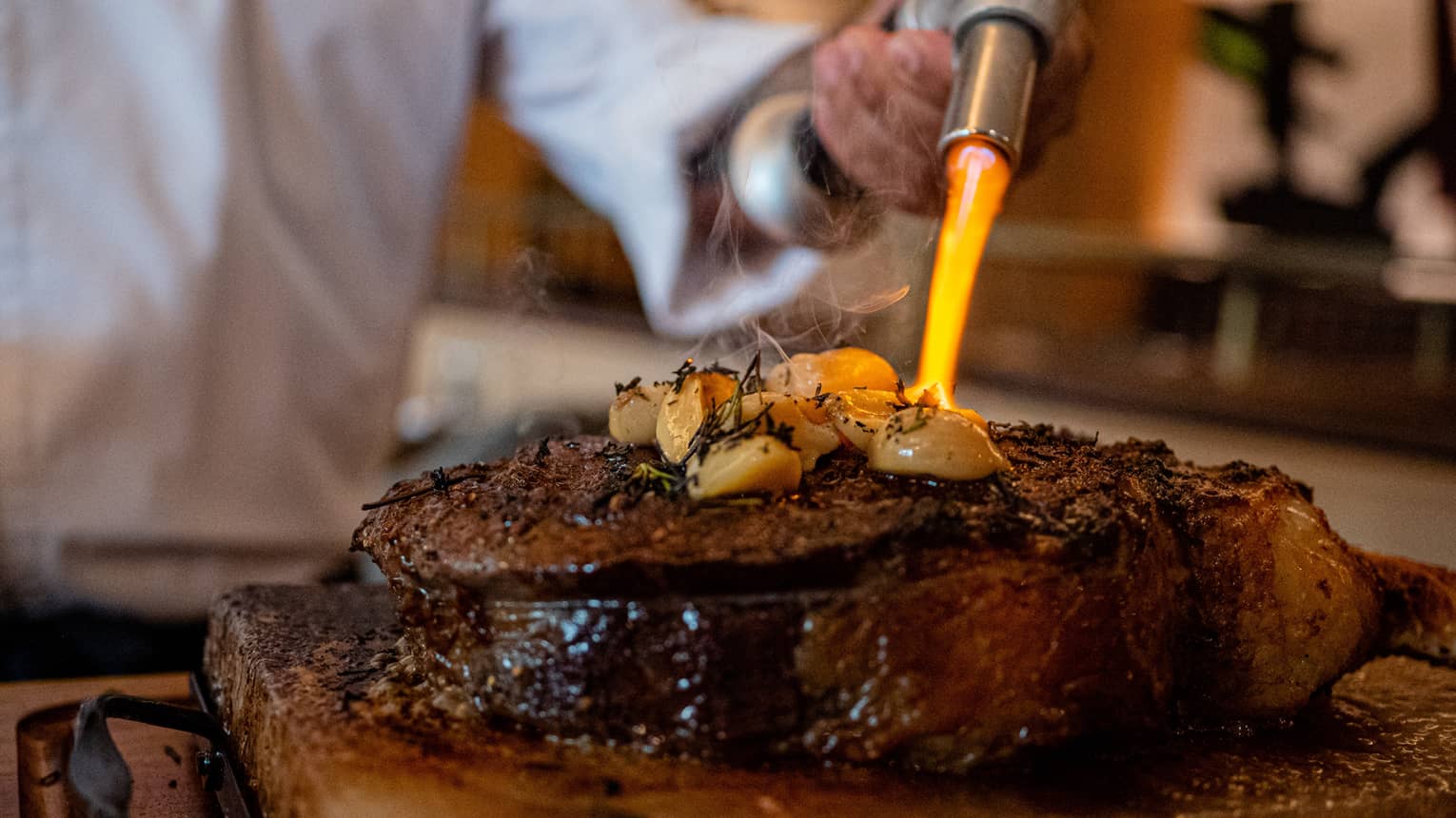 Chef with a torch, firing up a garlic-and-rosemary topped Tomahawk Steak at Ciclo.