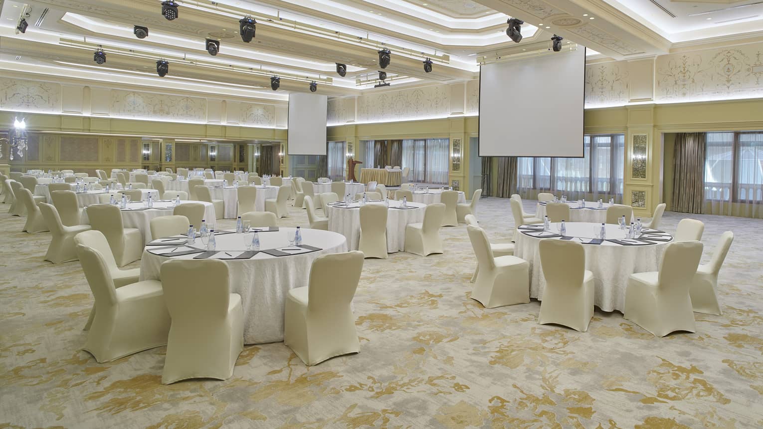 Large, neutrally decorated meeting room with vaulted lit ceiling, two rear screens and banquet seating