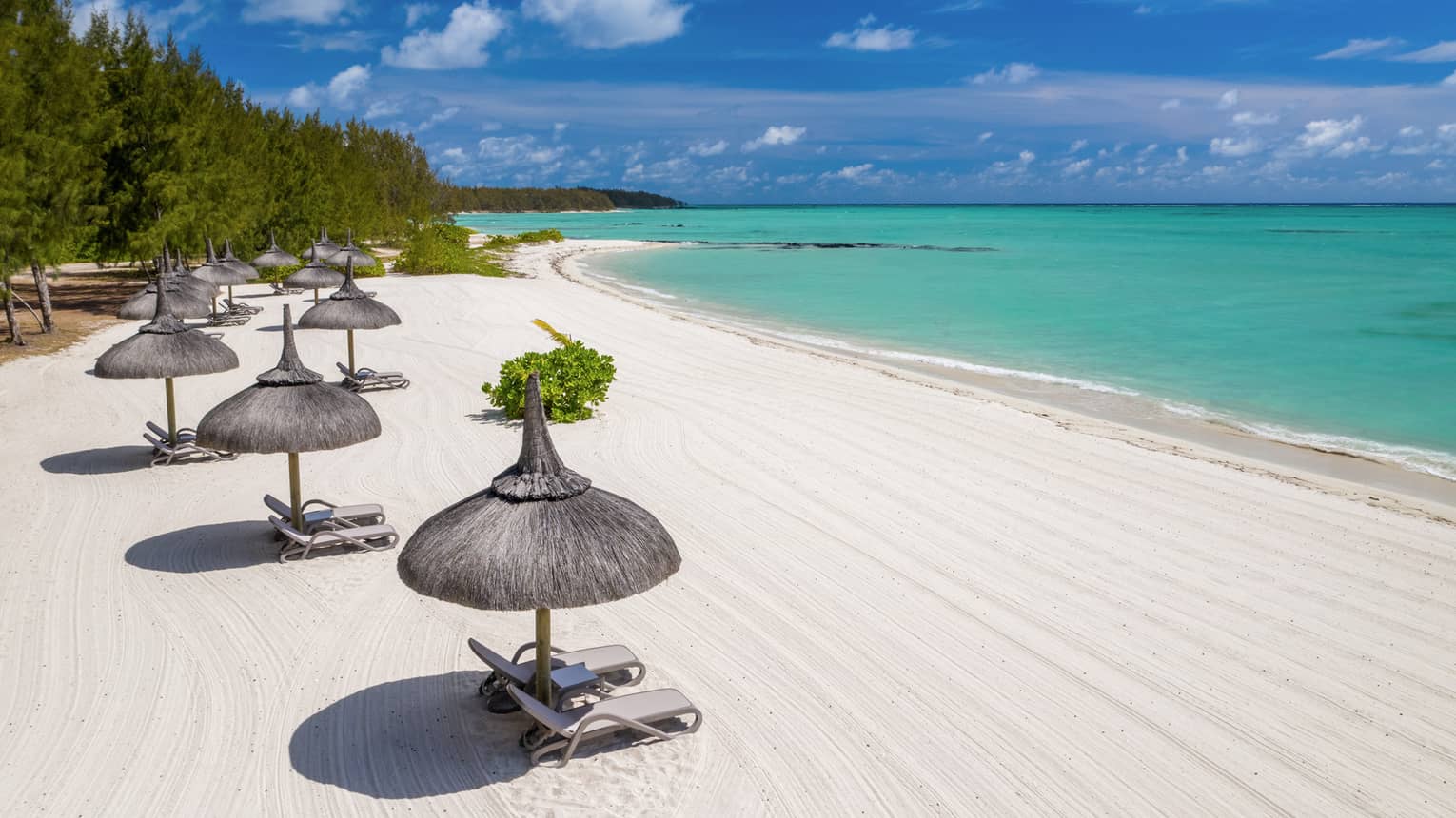 White sand beach with thatched umbrellas and lounge chairs and aqua ocean with blue sky above