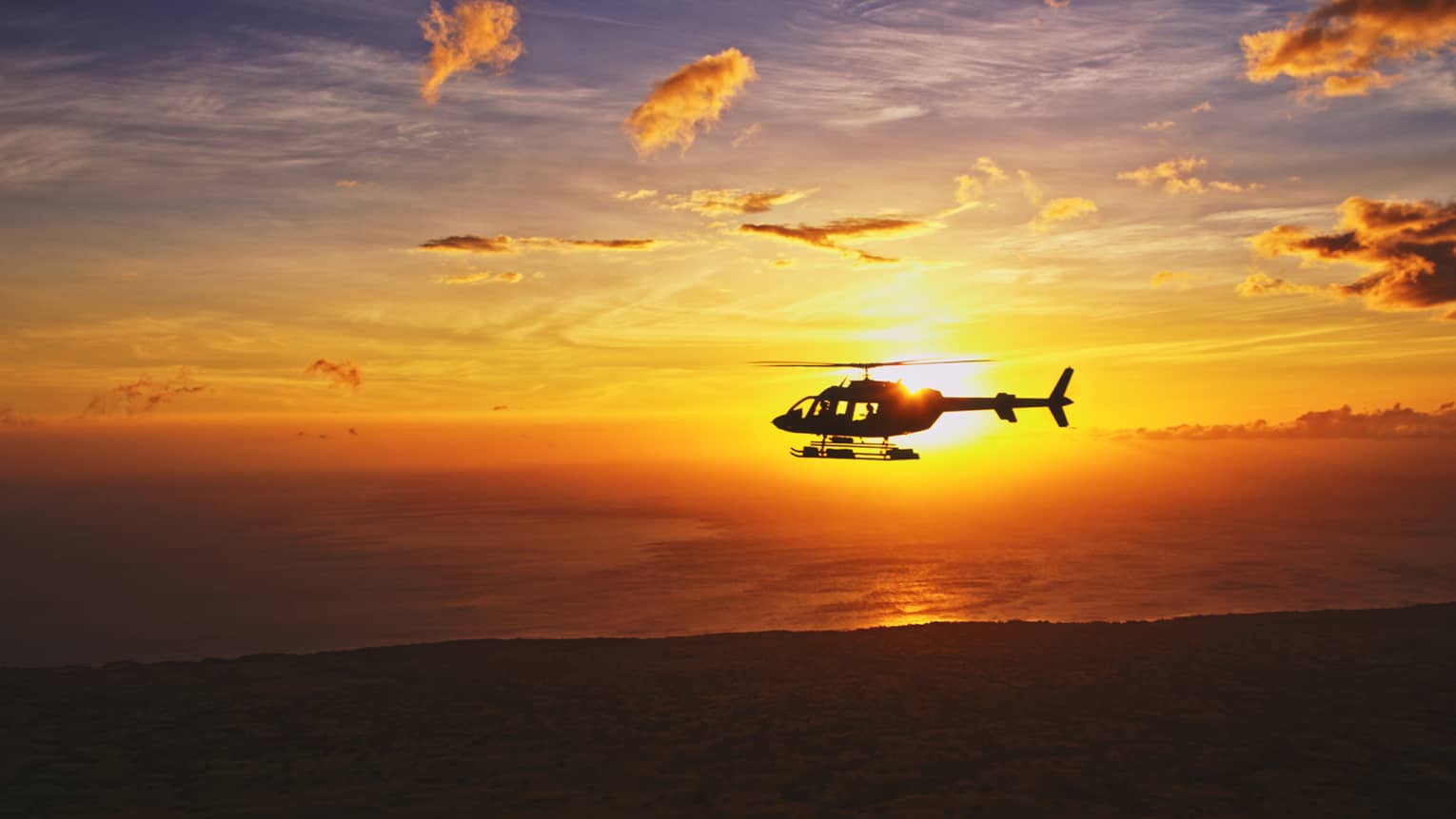 Silhouette of helicopter against orange sunset