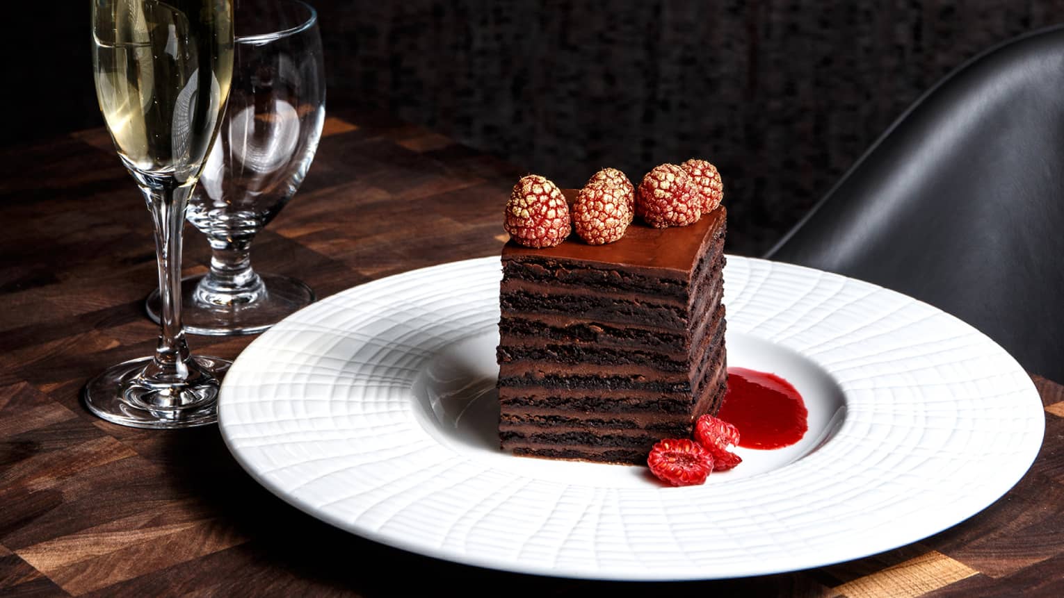 Layered chocolate desert on a white plate next to a flute of champagne and glass of water