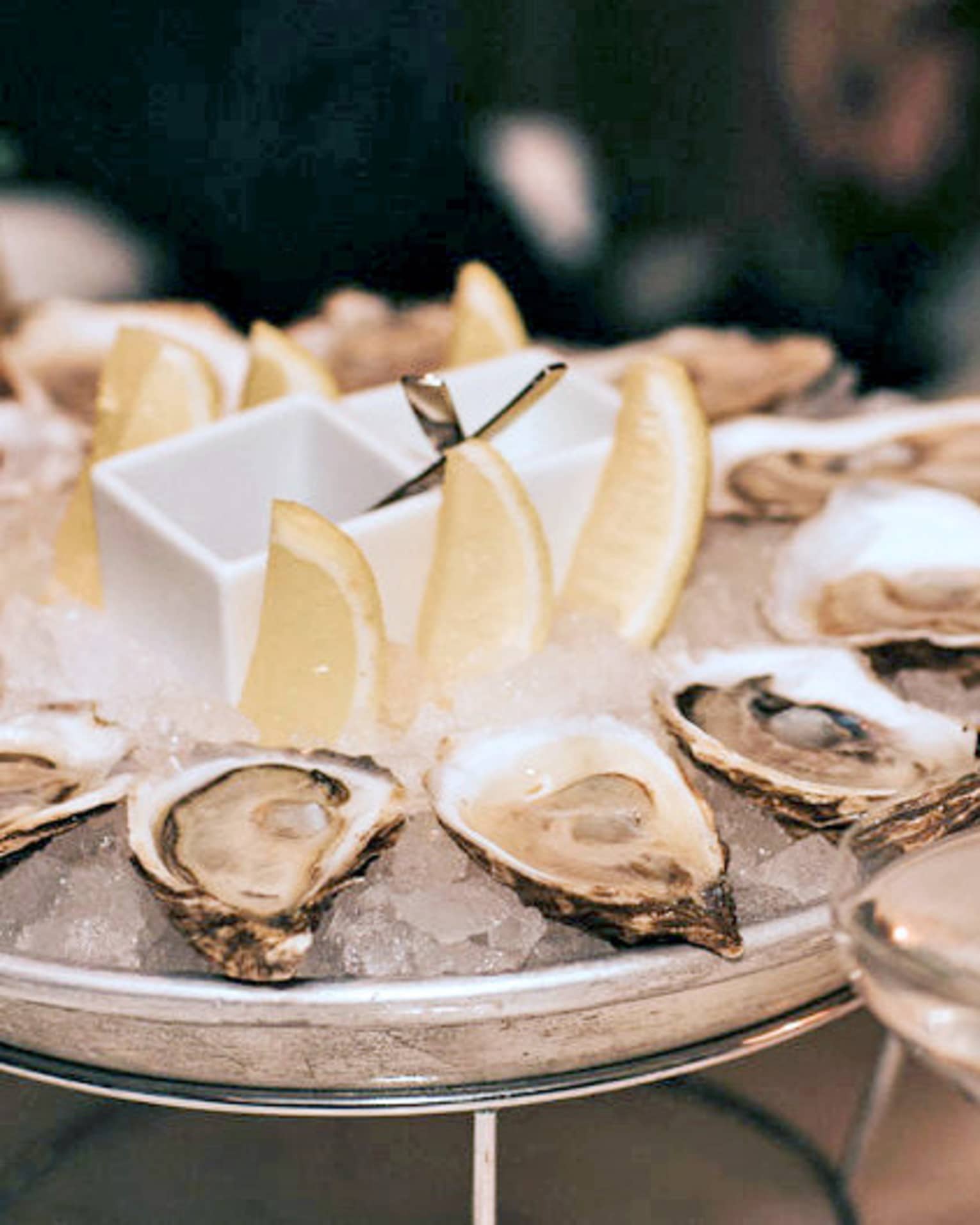 A dozen raw oysters around an ice platter with three lemon wedges in centre