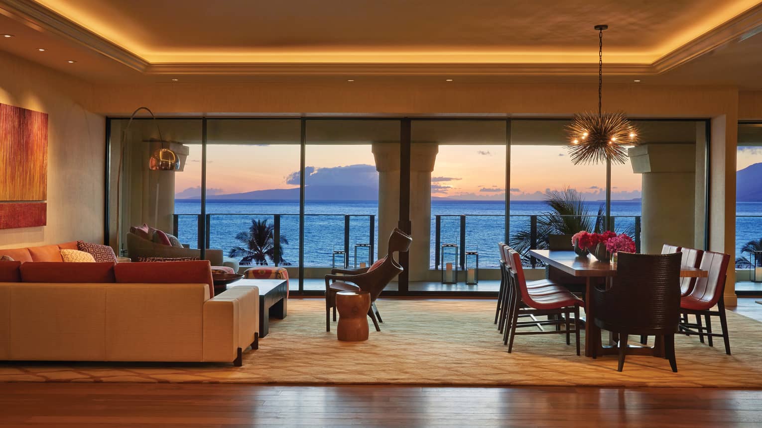 Maile Suite living area with beige and rust sectional, dining set, vaulted lit ceiling, ocean views out tall windows at sunset