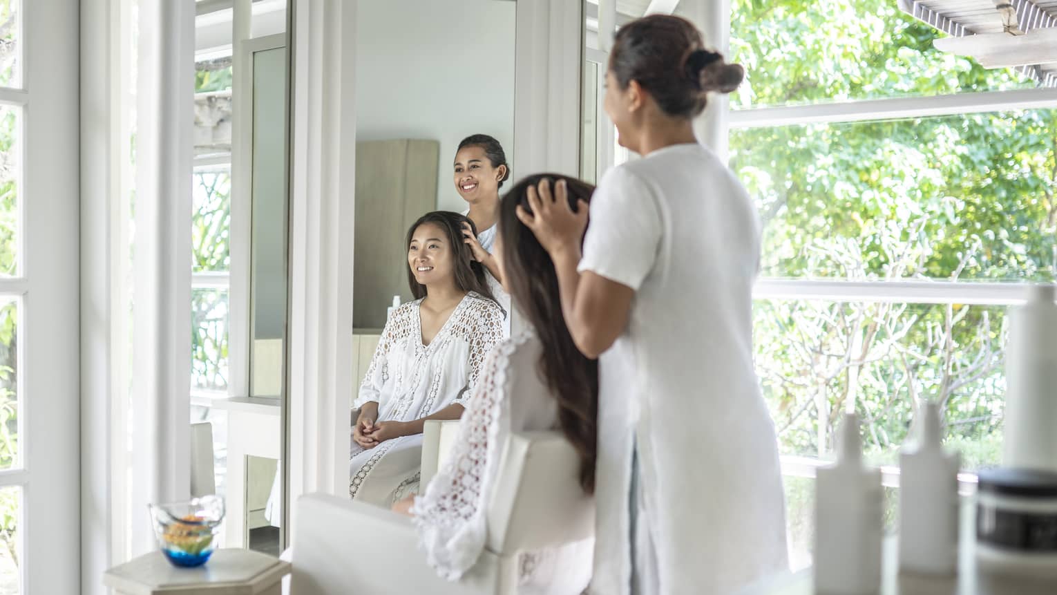 A four seasons guest gets her hair done while sitting in a white salon chair facing floor to ceiling windows revealing greenery just outside the salon