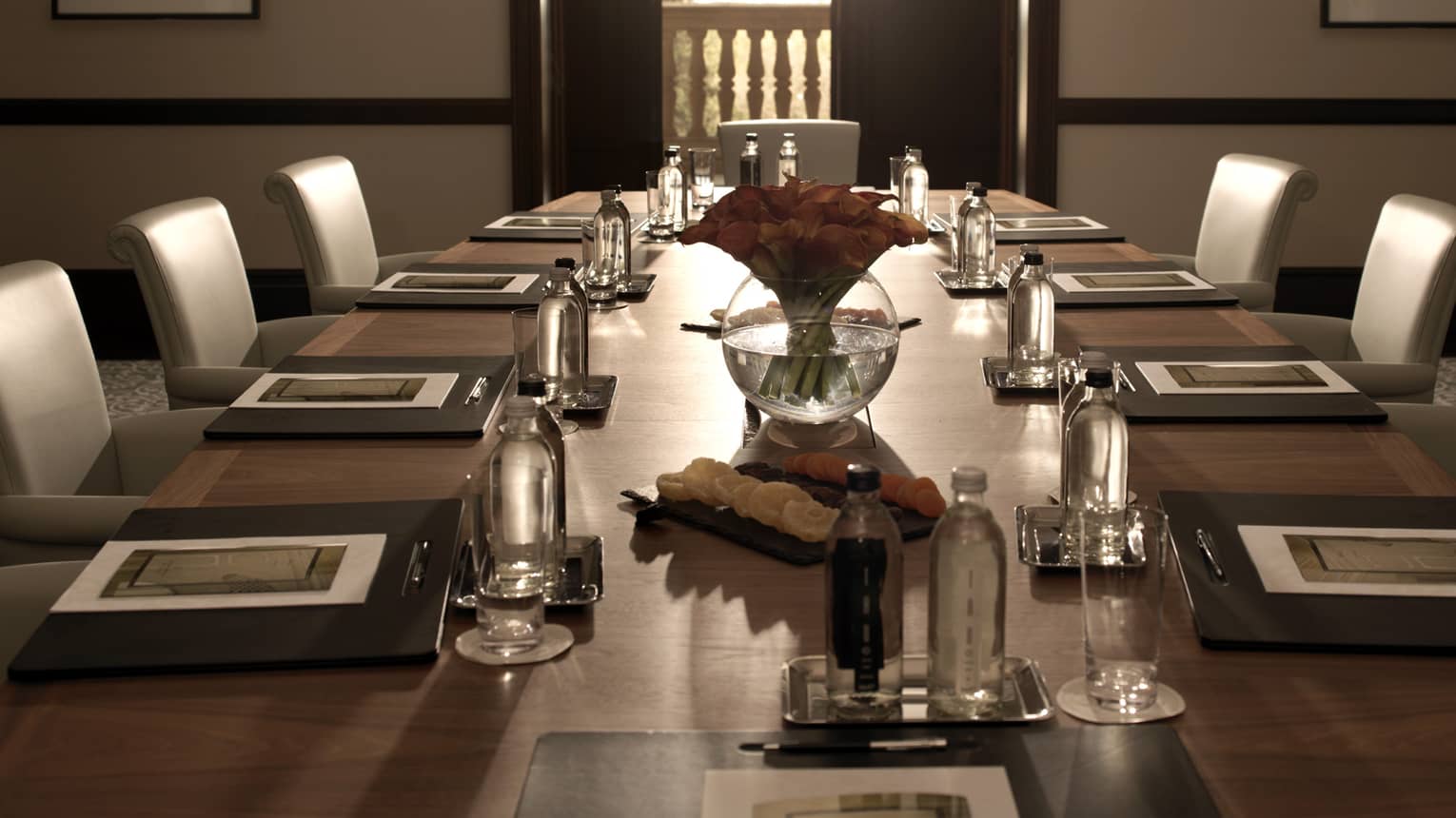 Sleek leather chairs around large, dark wood boardroom table set for business event 