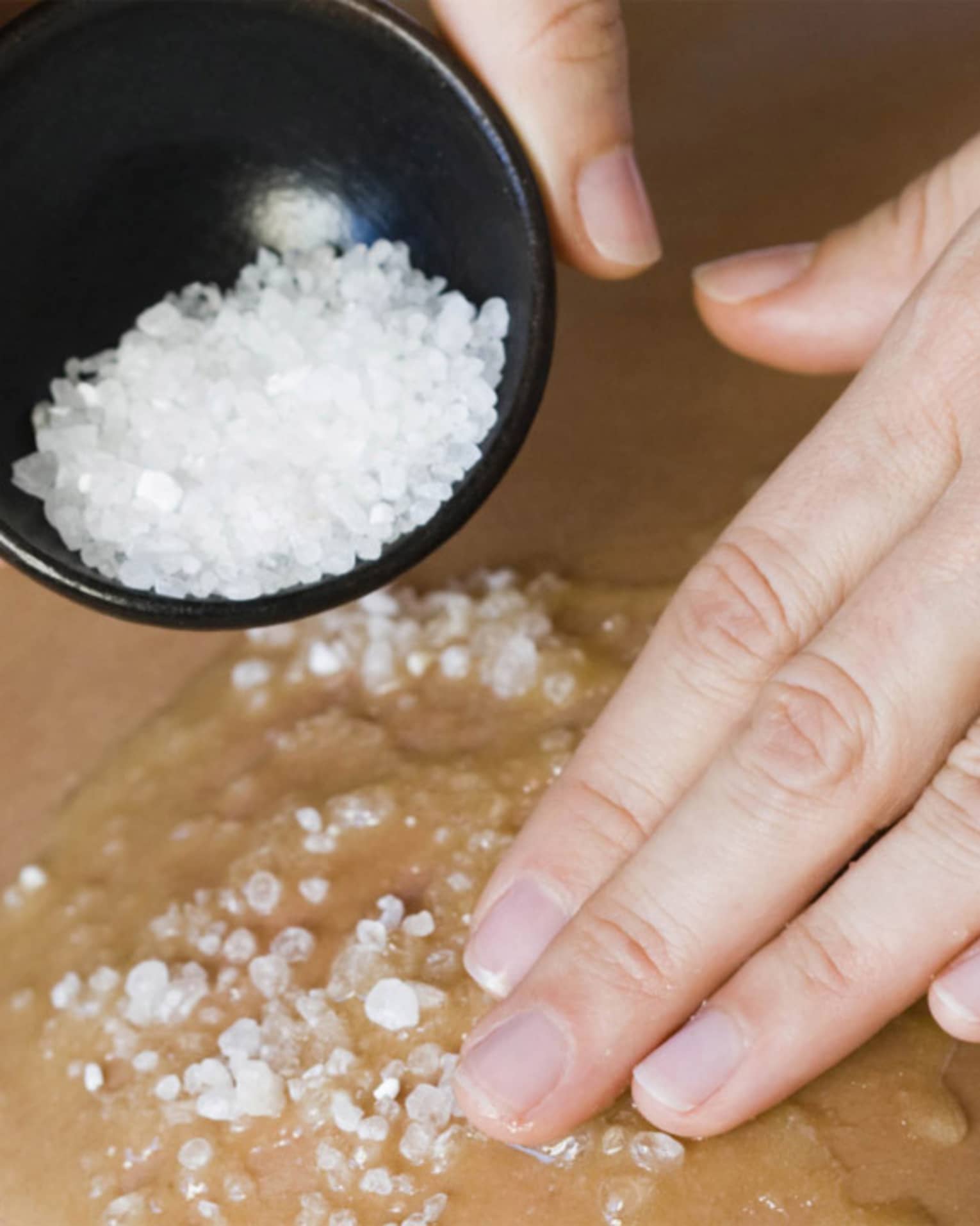 Close-up of large spa salts in bowl, hand rubbing crystals on bare back