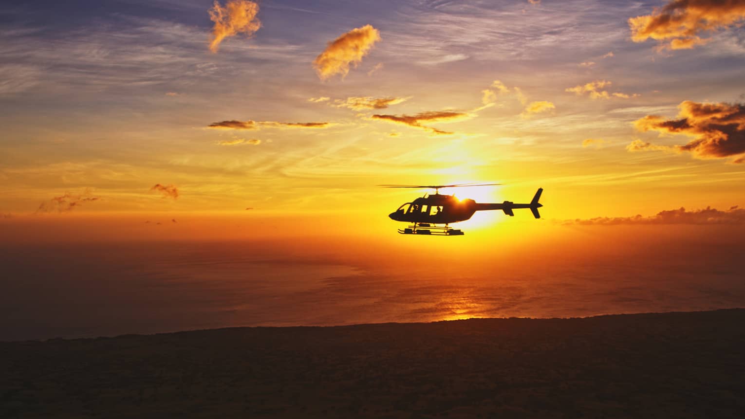 Silhouette of helicopter against orange sunset