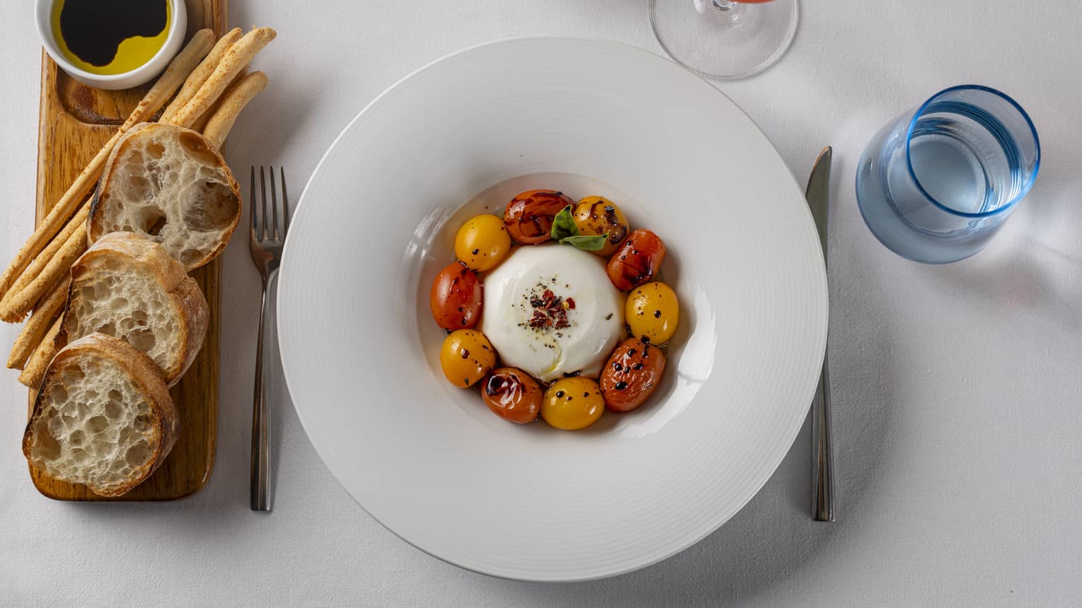 Burrata served with organic cherry tomatoes, fresh basil, extra virgin olive oil and chili flakes plated in a white, wide-rimmed bowl
