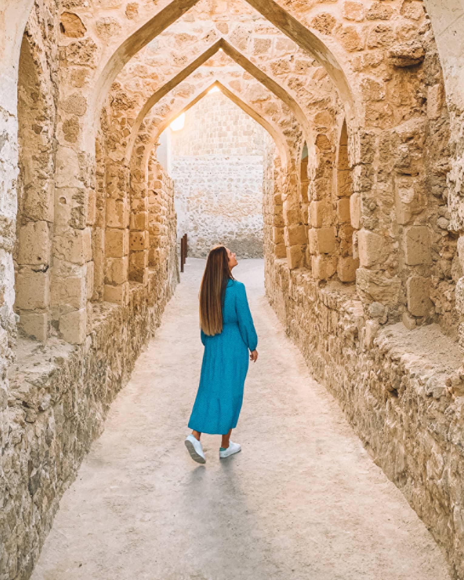 A woman stands underneath a stone pathway.