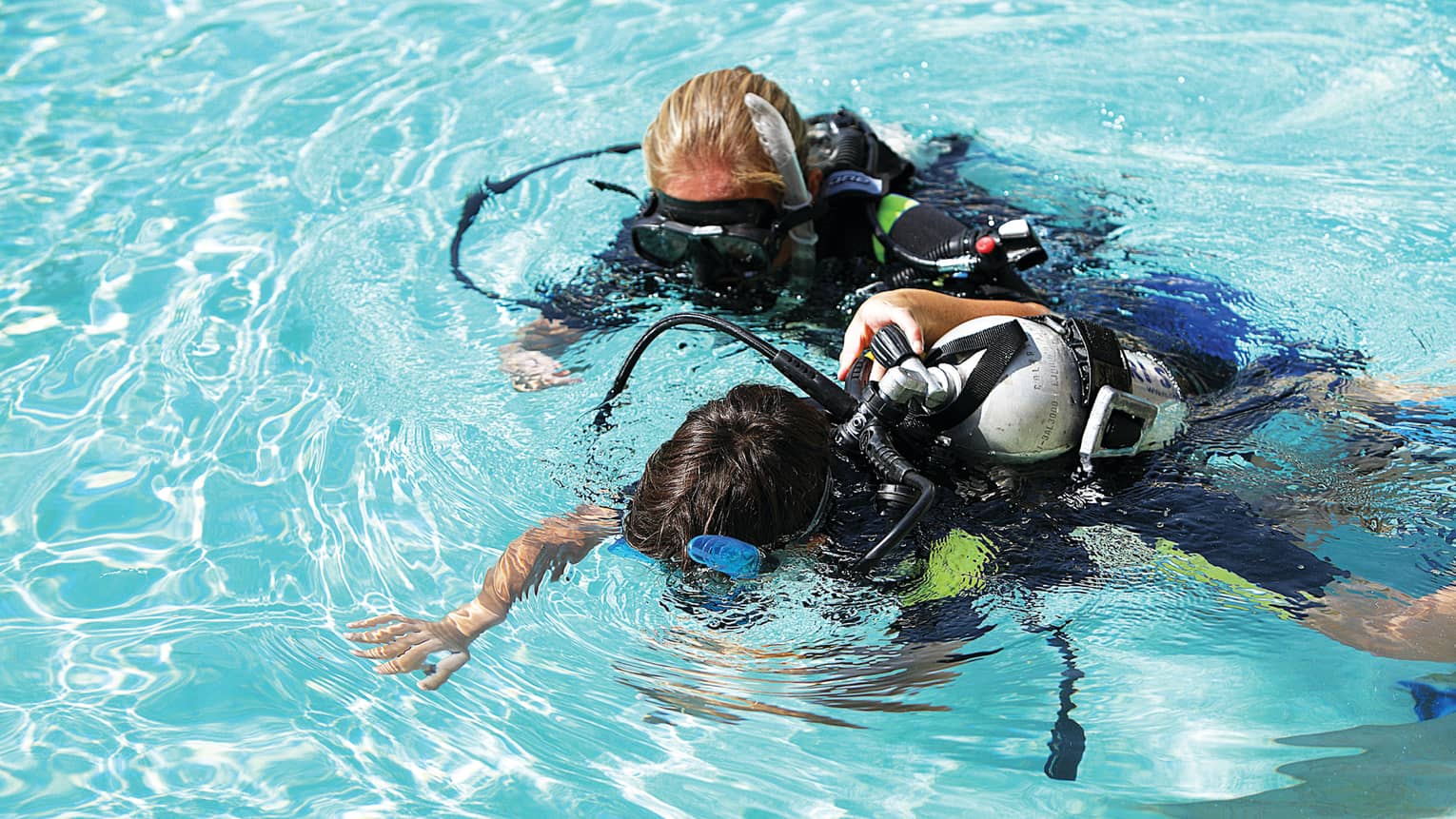 Two scuba divers look down into water 