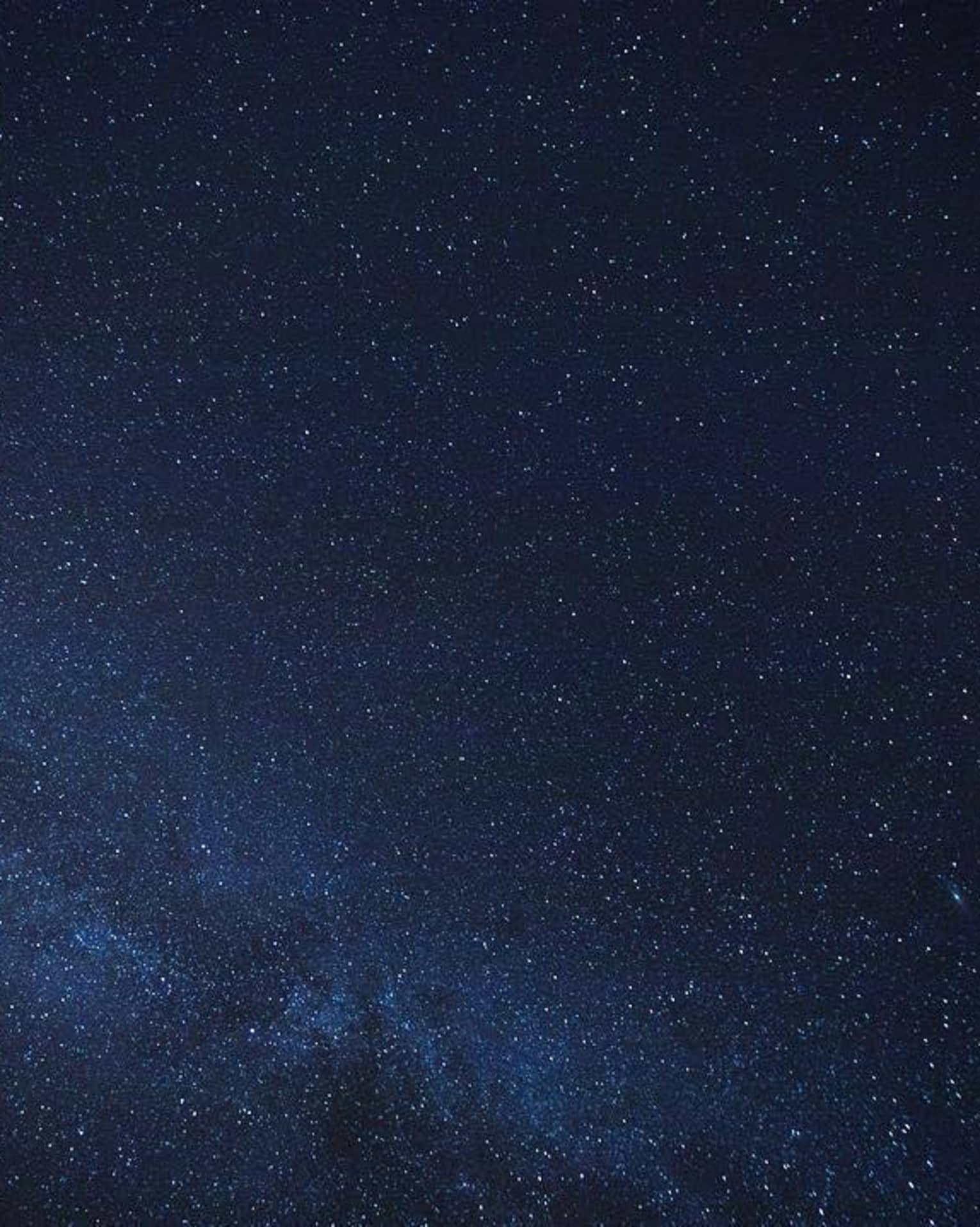 Thousands of stars dusting across a clear night sky; a cluster of stars form the Milky Way, just barely visible in the sky.