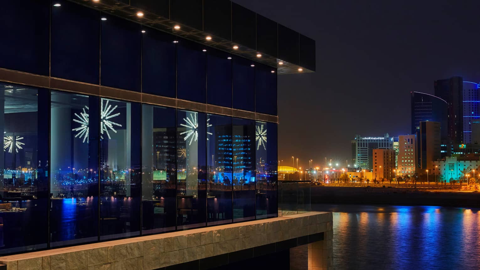 Exterior view of glass windows of CUT by Wolfgang Puck restaurant at night, modern white chandeliers visible