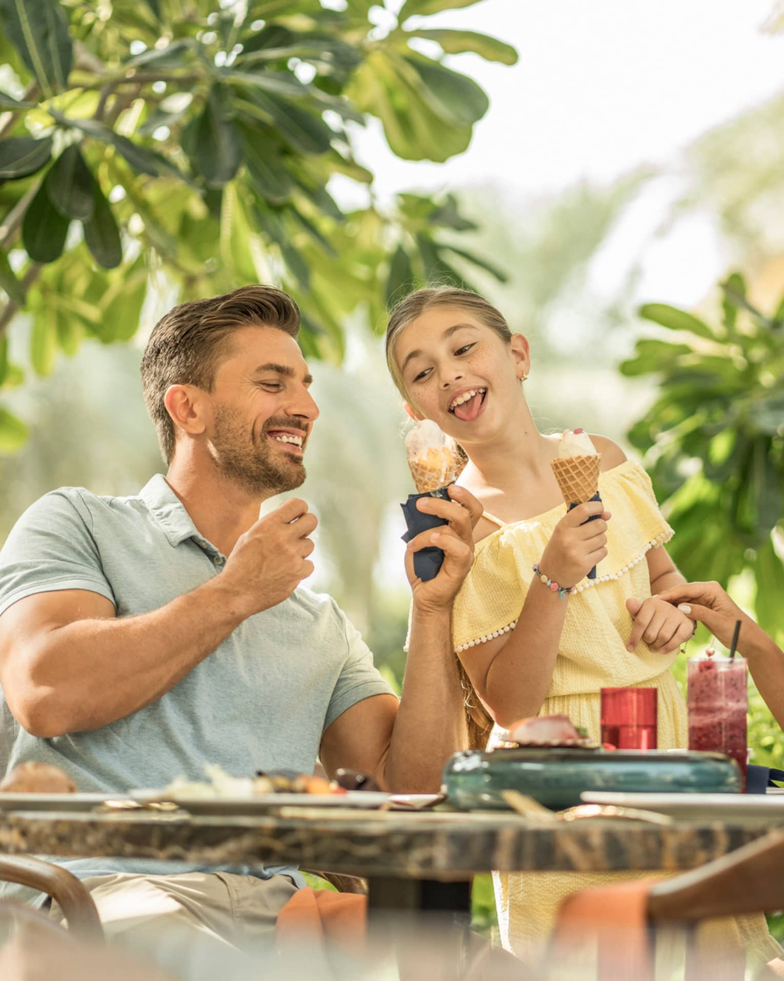 ,A man and young girl eat ice cream cones, while two ladies sitting across from them sip on cocktails