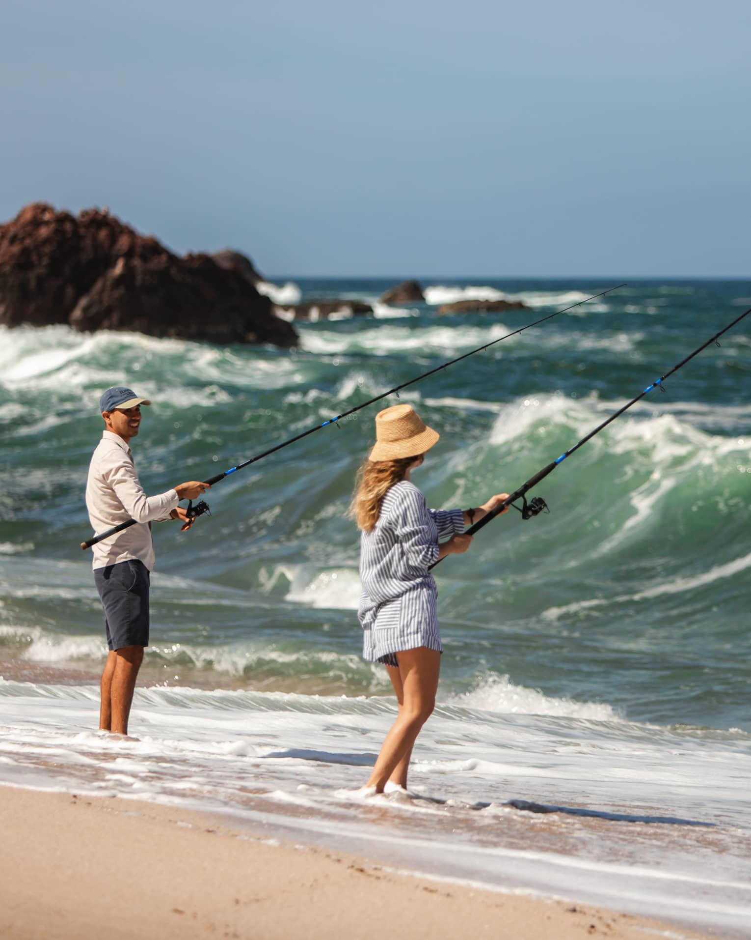 Two people fishing on a beach shore.