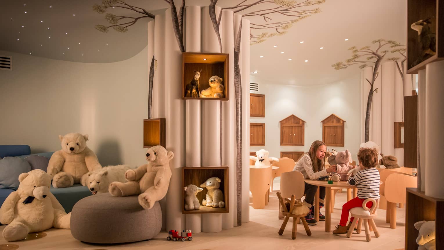Kids play with toys at small table near chairs, stuffed bears in Kid Kingdom playroom
