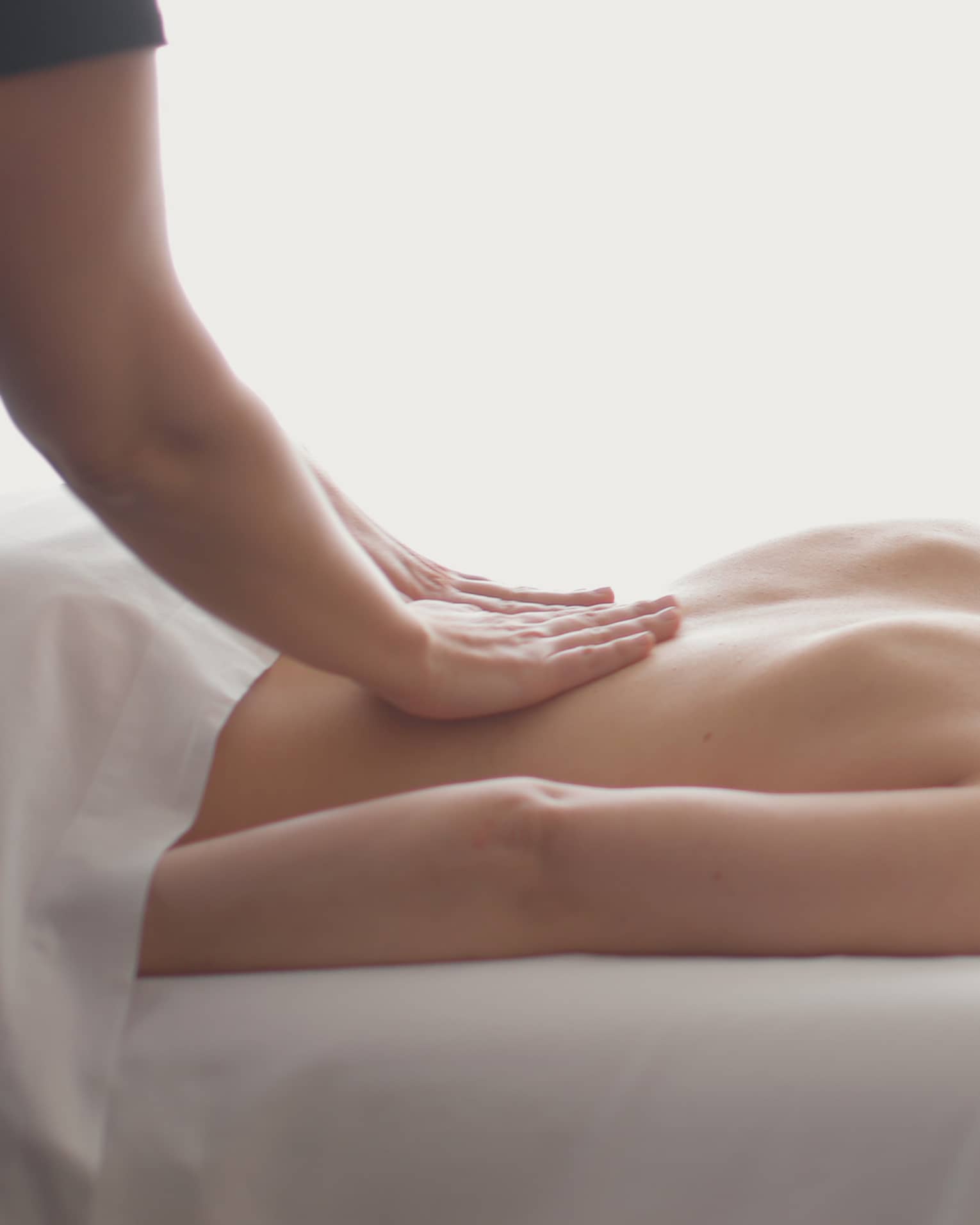Side view of woman lying on massage table, hands massaging her bare shoulders