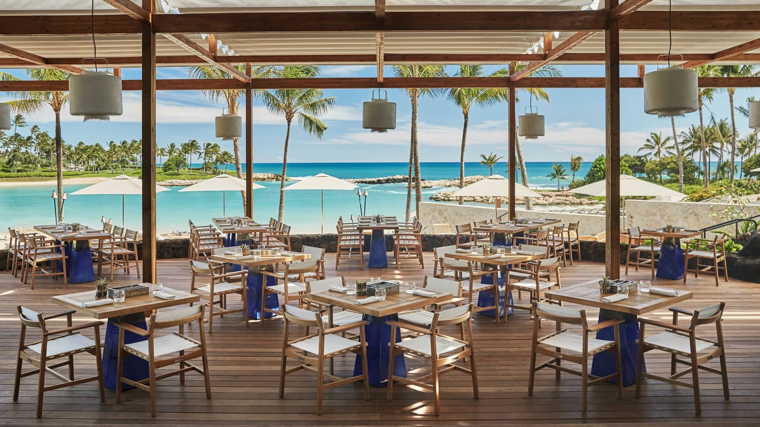 Large dining room under wood pergola on patio overlooking turquoise lagoon