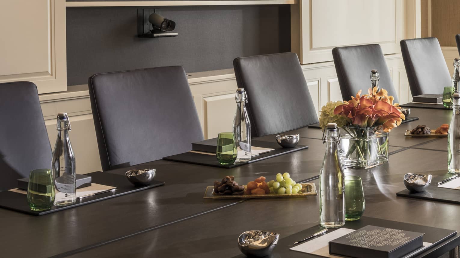 Long boardroom table set with glass bottles of water, flowers in bright meeting room