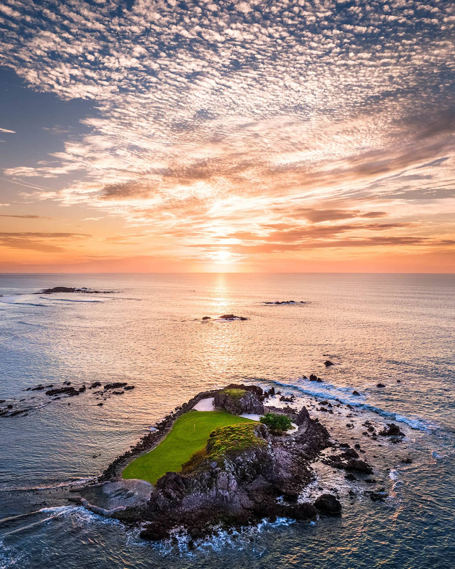 A small island that is part of a gold course, the sun is rising in the distance.